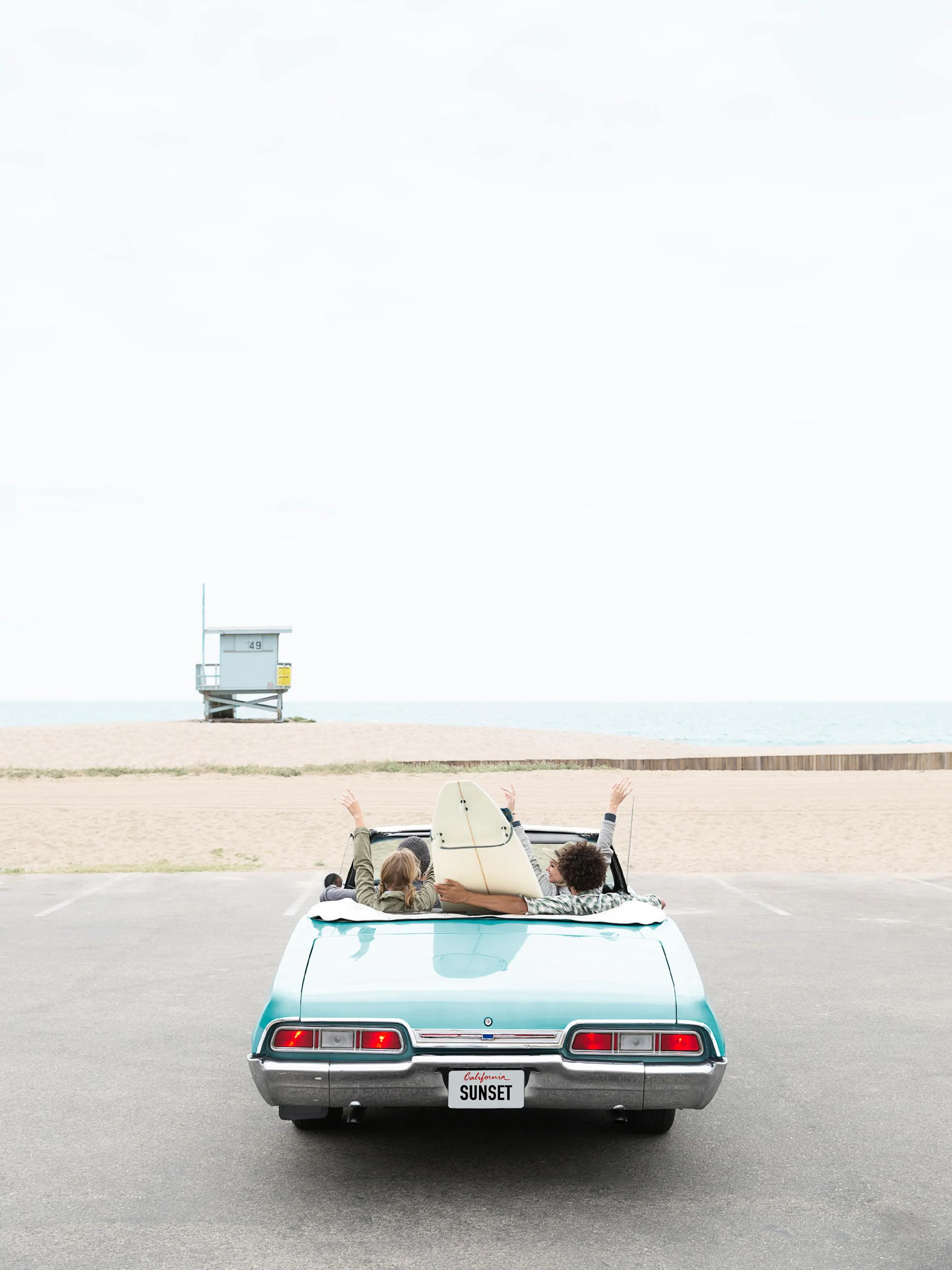 Poster: Türkises Oldtimer-Cabrio mit Surfern und Surfbrett am Strand, Blick auf Meer und Rettungsturm.