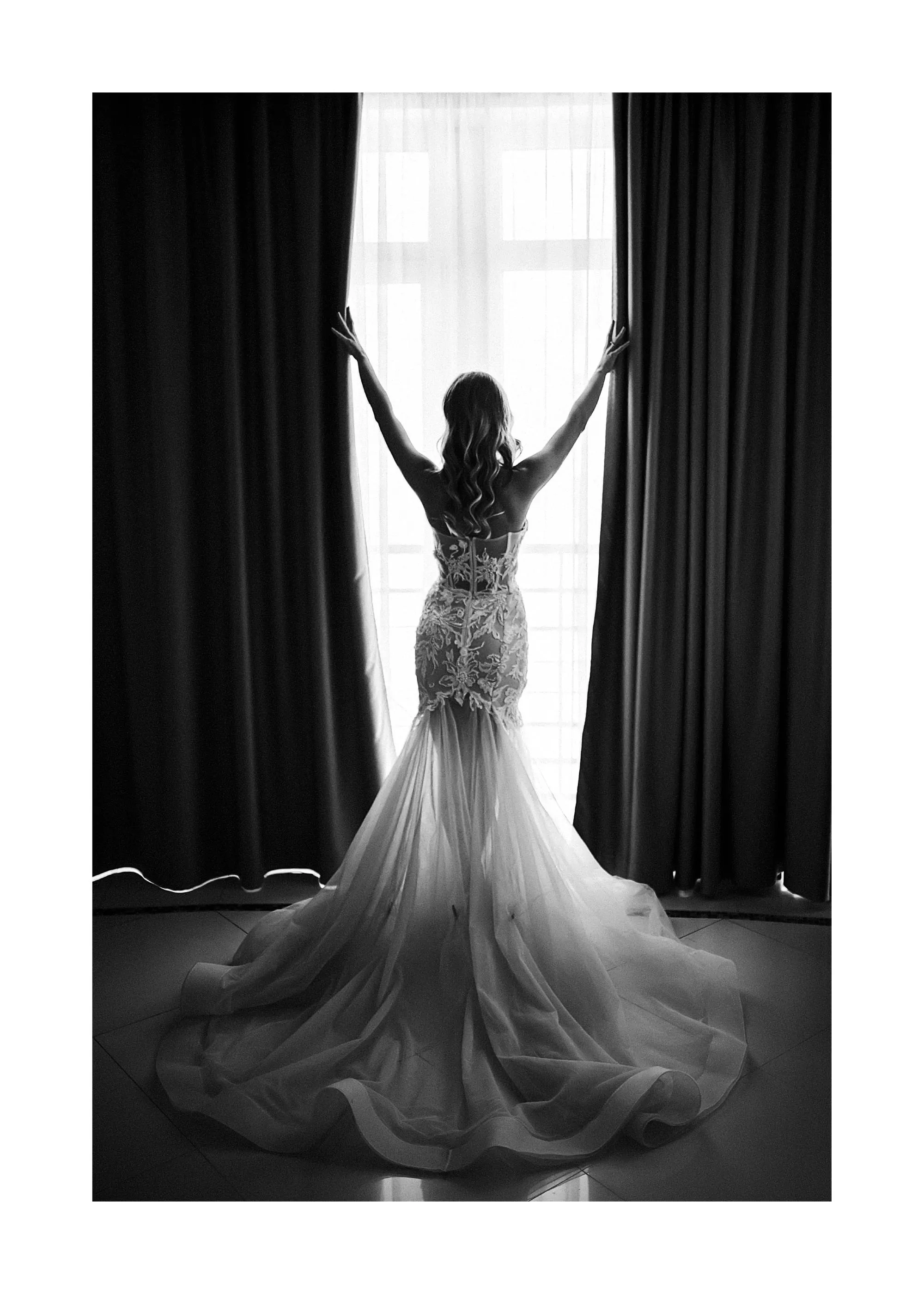 Poster en noir et blanc dune mariée de dos, bras levés, ouvrant des rideaux sur une fenêtre lumineuse.