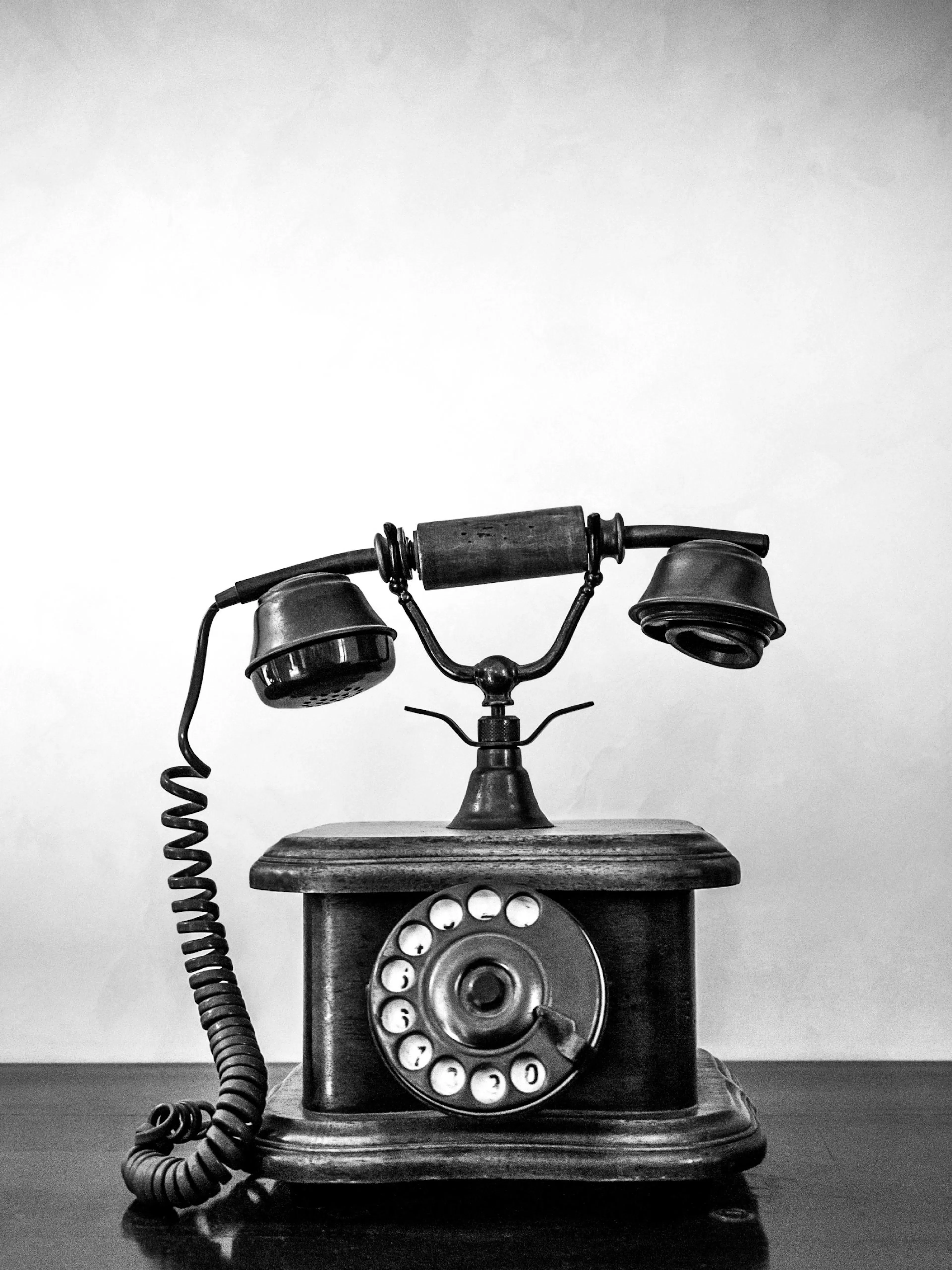 En sort-hvid plakat af en vintage telefon i træ, med en drejeskive og en spiralledning.