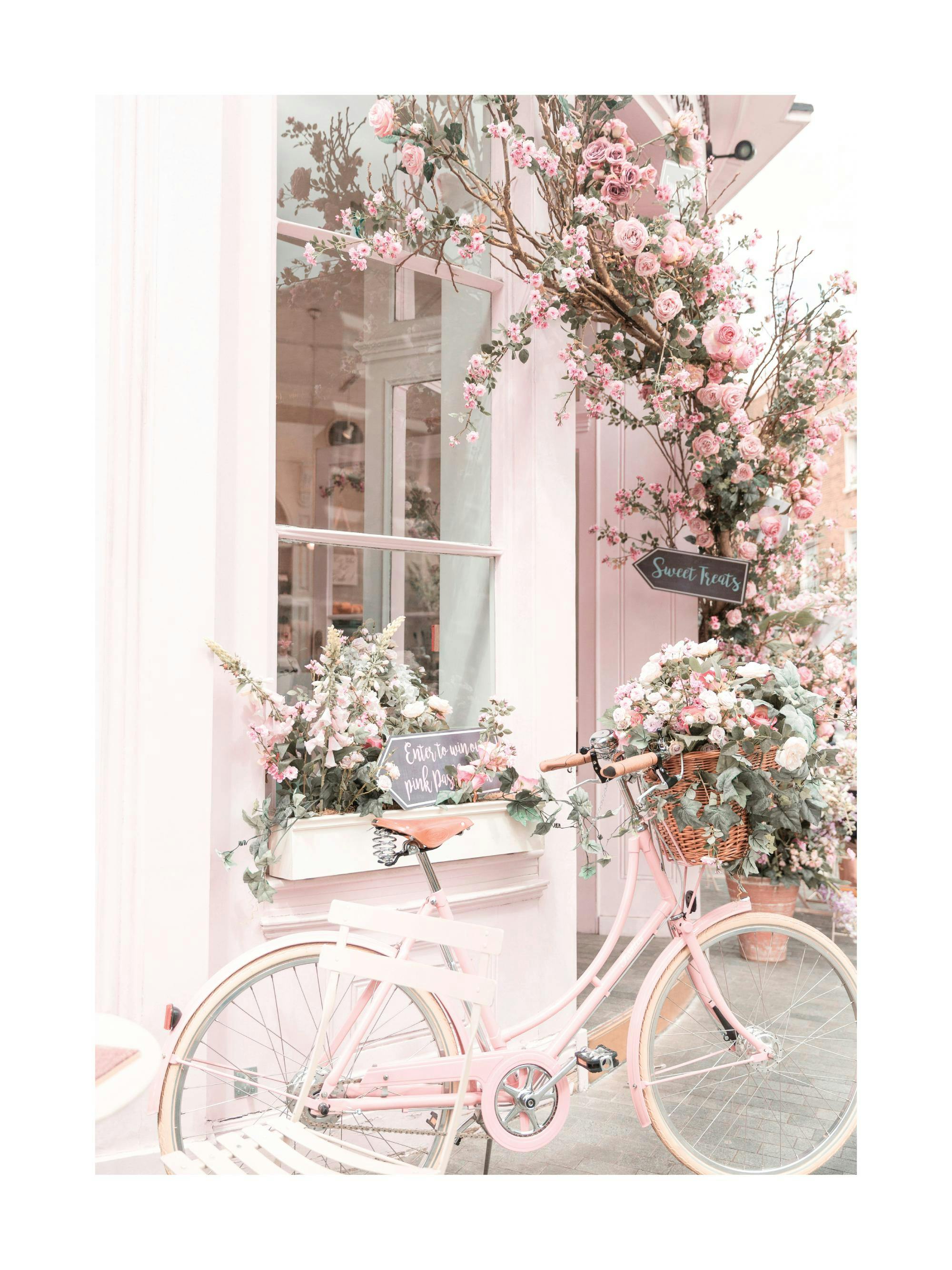 Un poster dun vélo rose pastel devant une boutique décorée de fleurs roses et blanches, avec un panneau Sweet Treats.