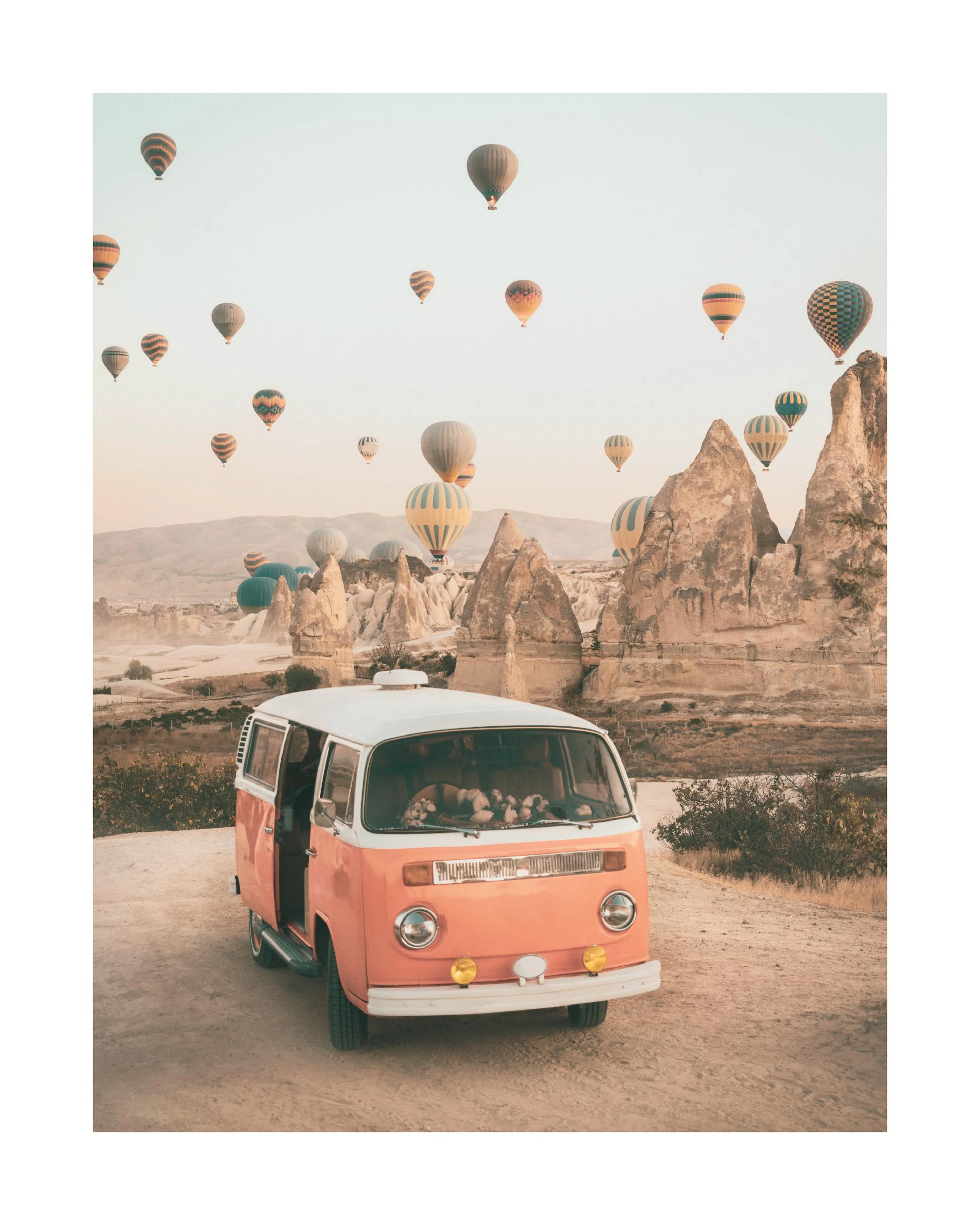 A poster featuring a vintage orange and white camper van on a dirt road, with numerous hot air balloons floating above rock form