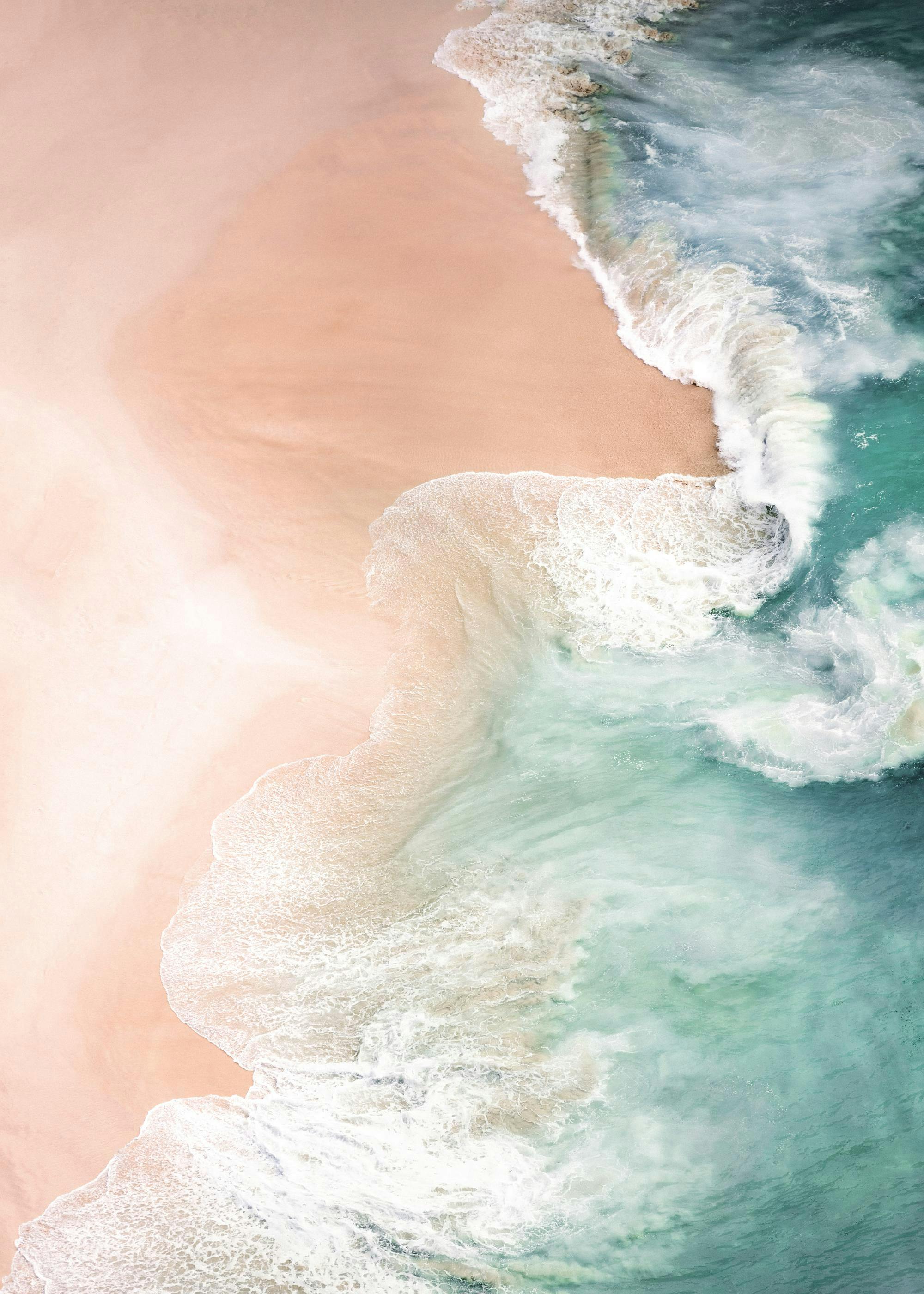 Póster de una playa de arena rosada con olas turquesas y espuma blanca, visto desde arriba.