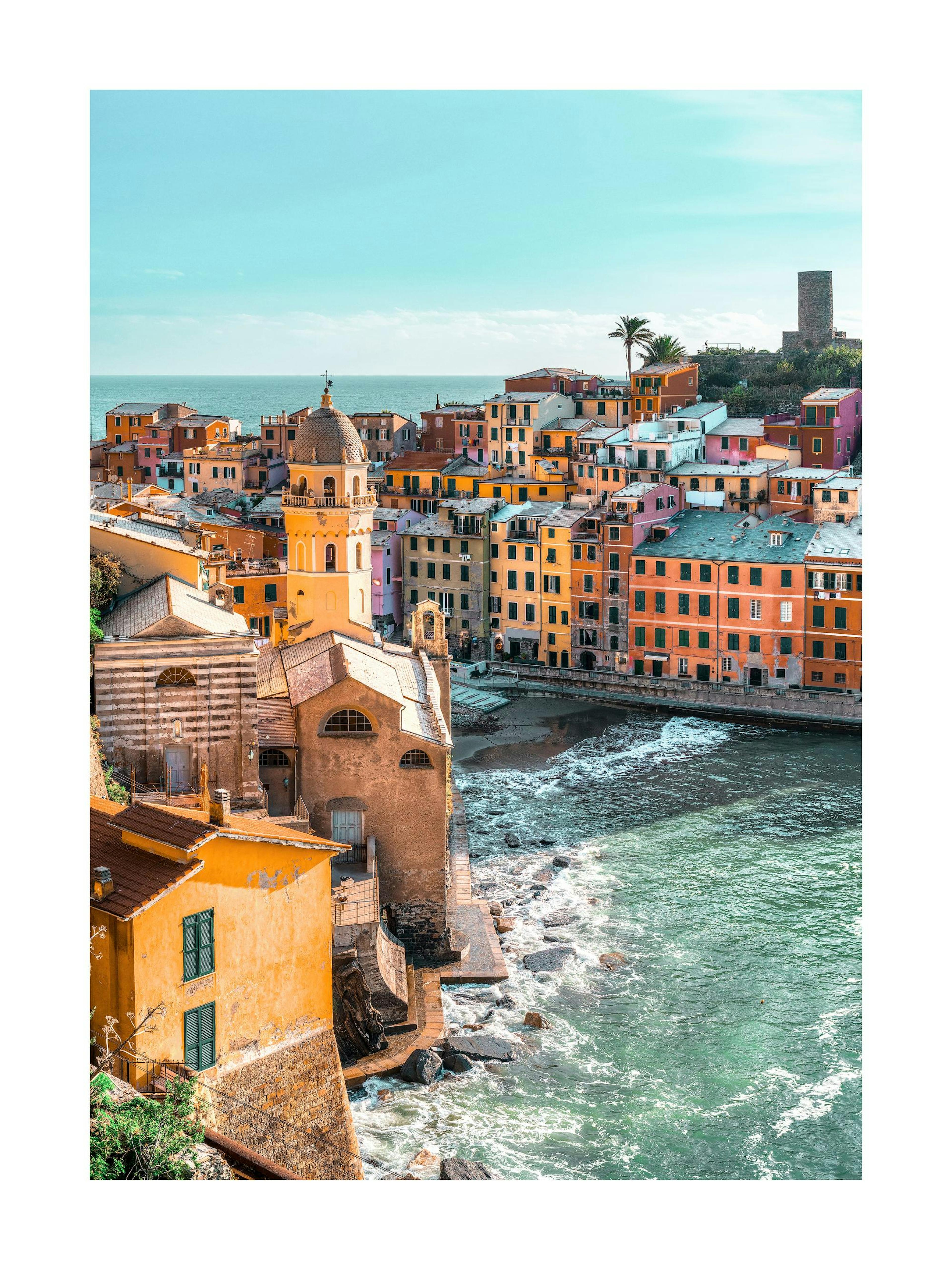 A stunning poster of the colorful Italian coastal village of Vernazza with a church and waves crashing against the shore.