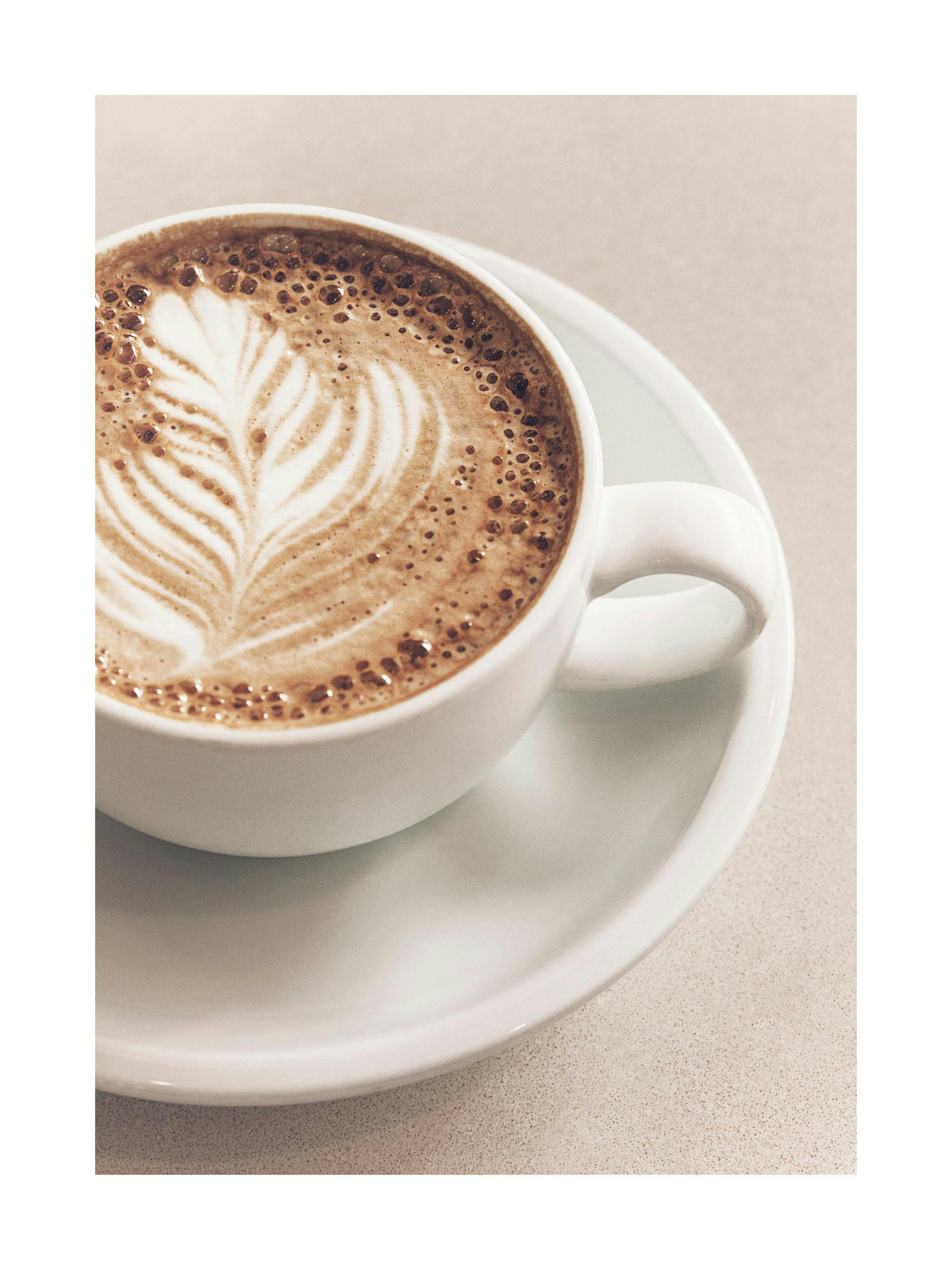 A poster featuring a close-up of a white cup of coffee with latte art on a light-colored surface.