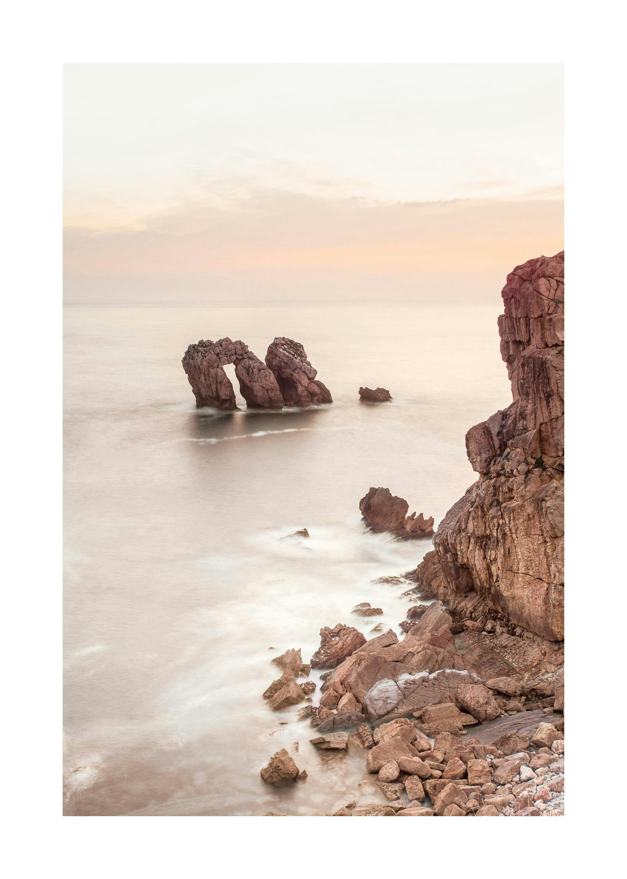 Poster du littoral rocheux avec des arches naturelles dans leau calme et un ciel pastel à laube.