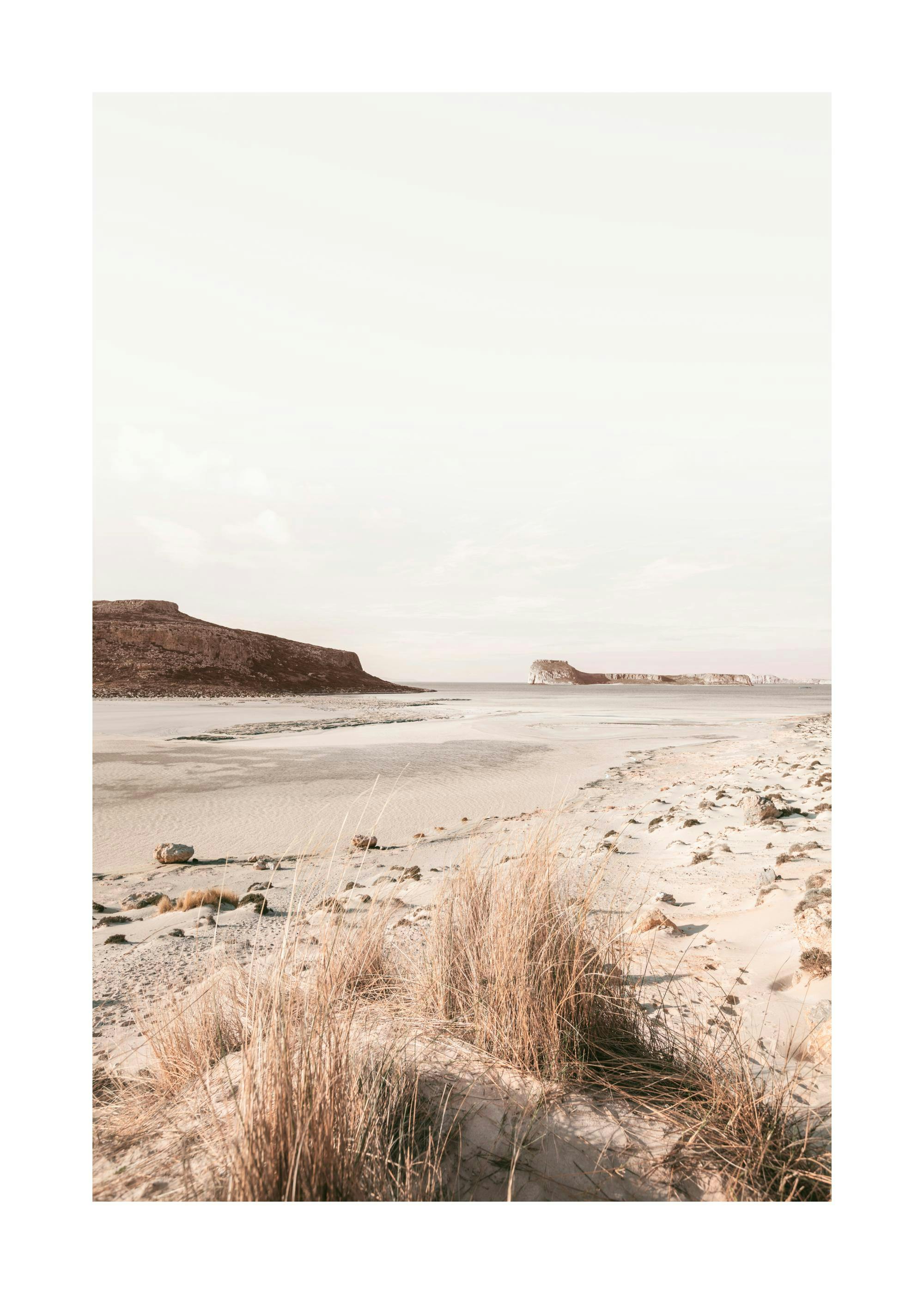 A poster featuring a vast sandy beach with dry grasses in the foreground leading to calm water and distant mountains under a pal
