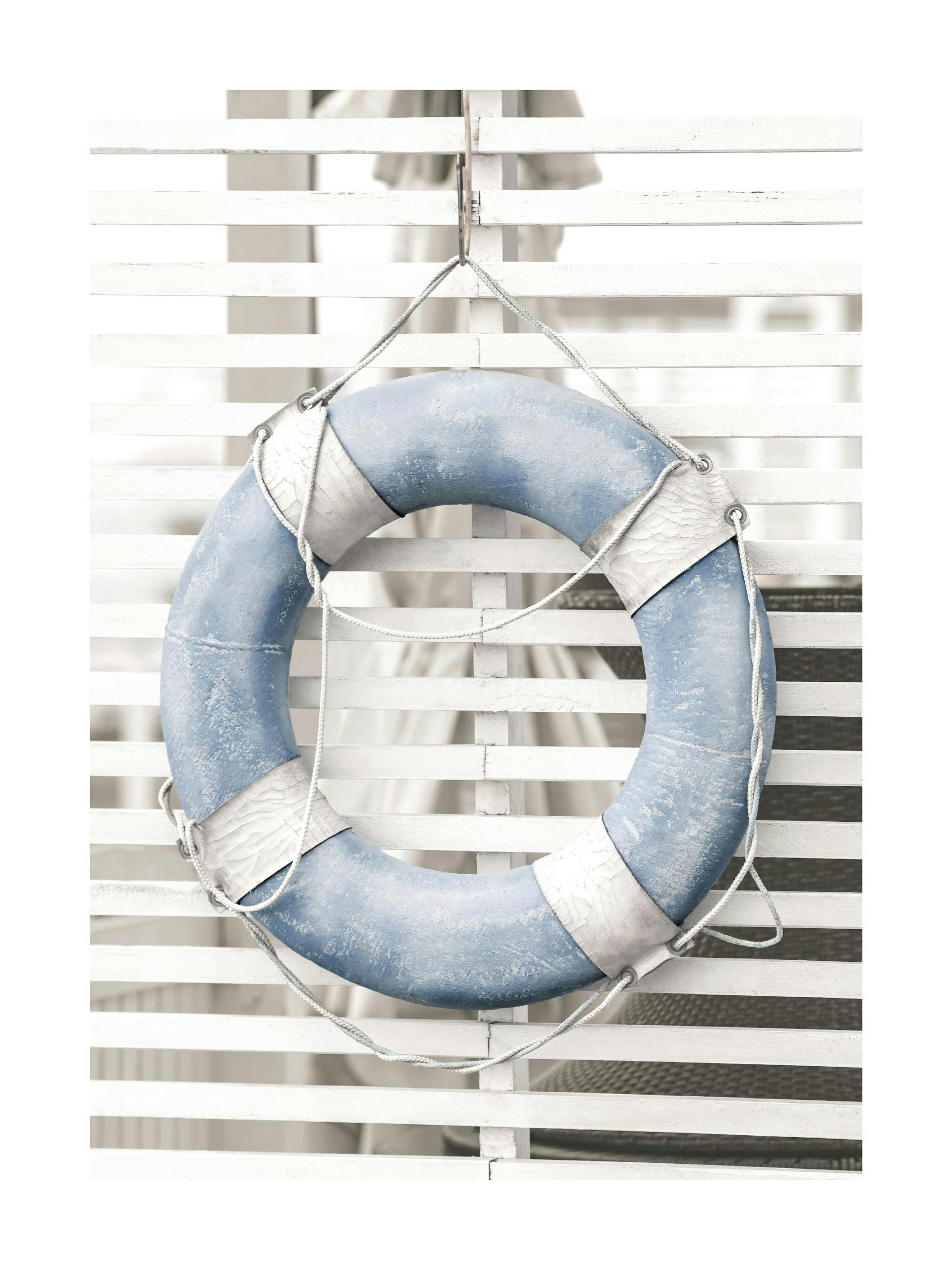 A poster featuring a weathered blue life preserver with white straps and rope, hanging on a white slatted fence.