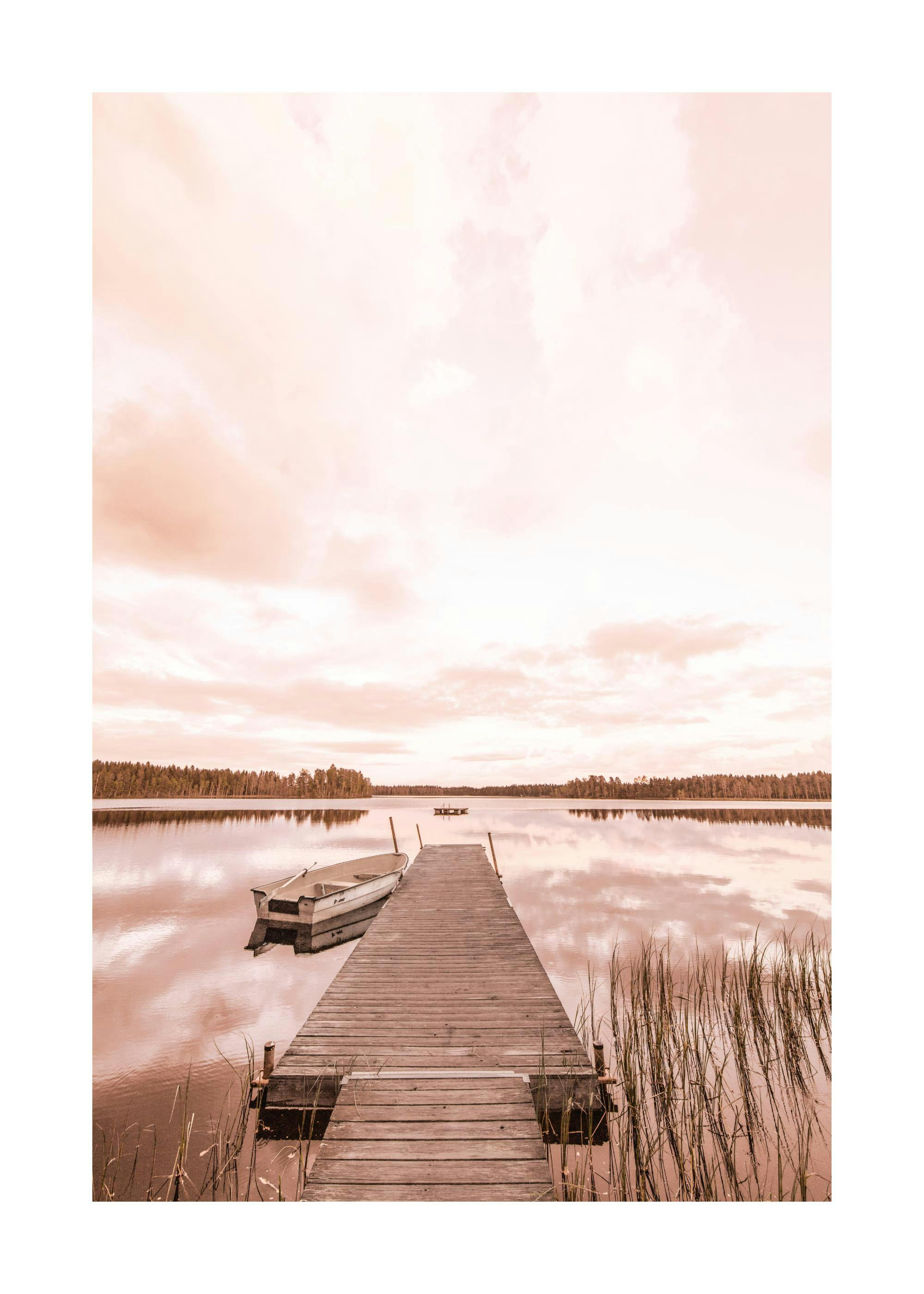 Póster de un muelle de madera y un bote en un lago tranquilo con un cielo rojizo y nubes reflejadas en el agua.