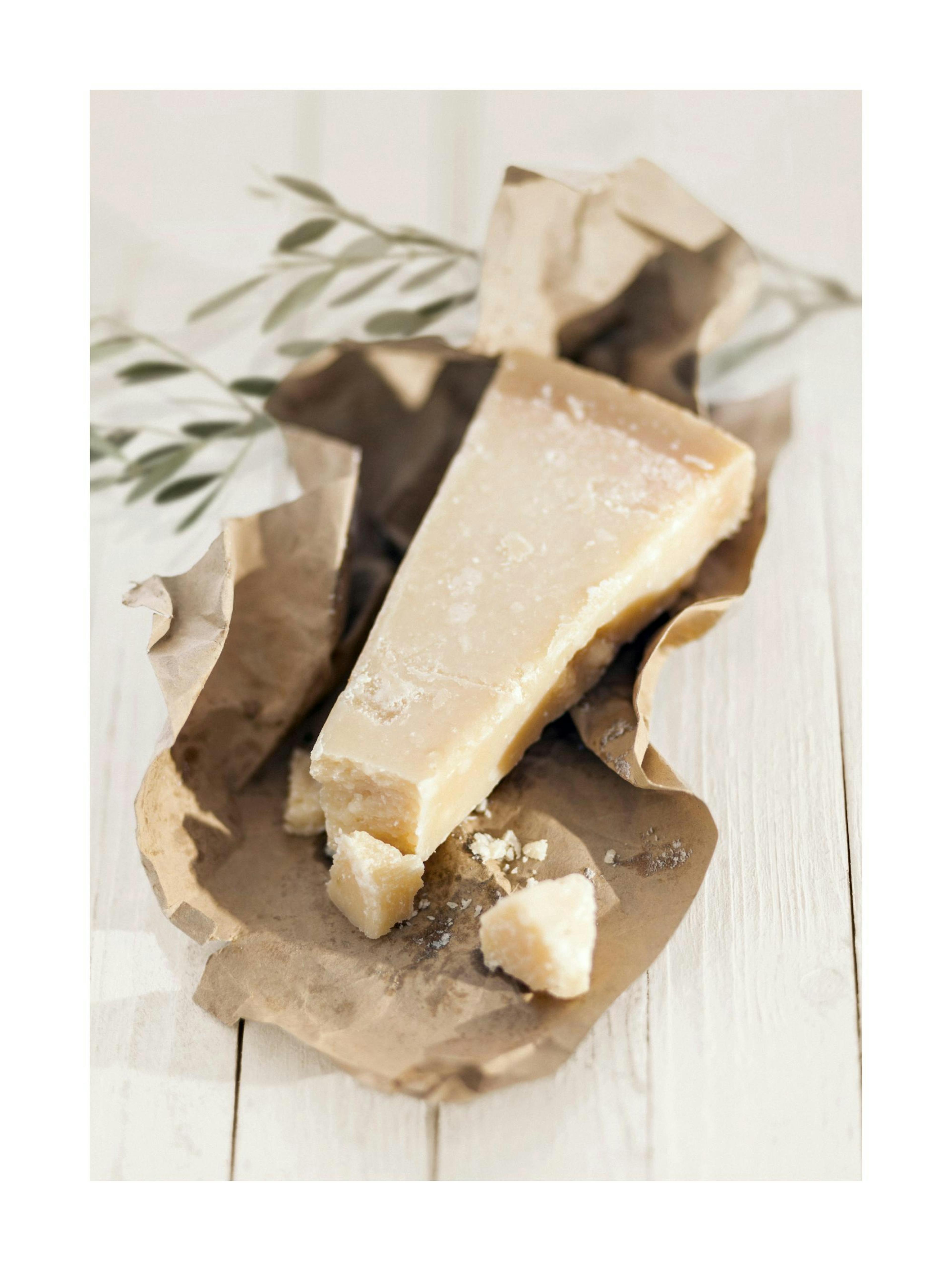 A poster featuring a wedge of parmesan cheese on brown paper, with an olive branch in the background.