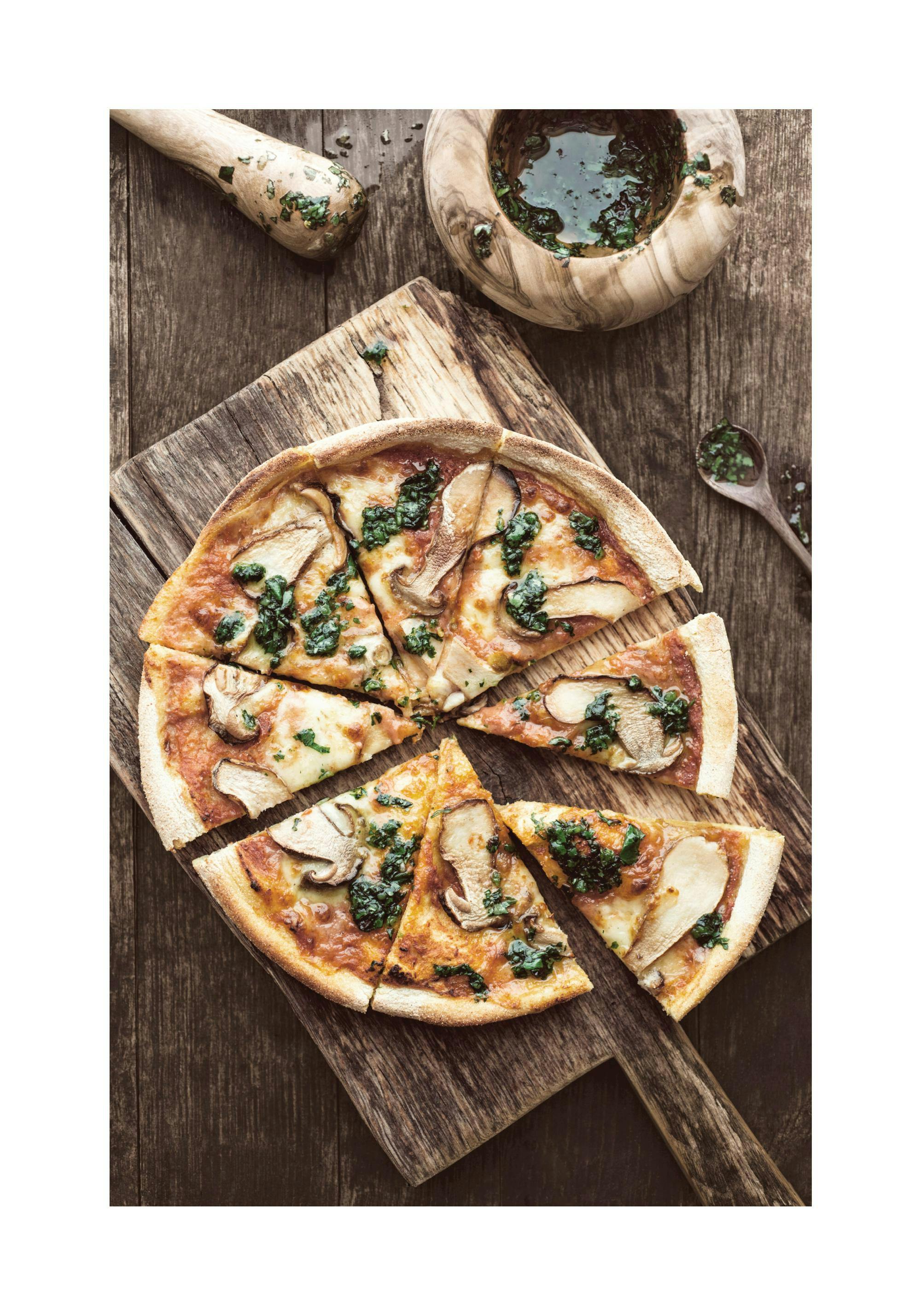 A top-down poster of a sliced pizza with mushrooms and spinach on a wooden board, next to a mortar and pestle.