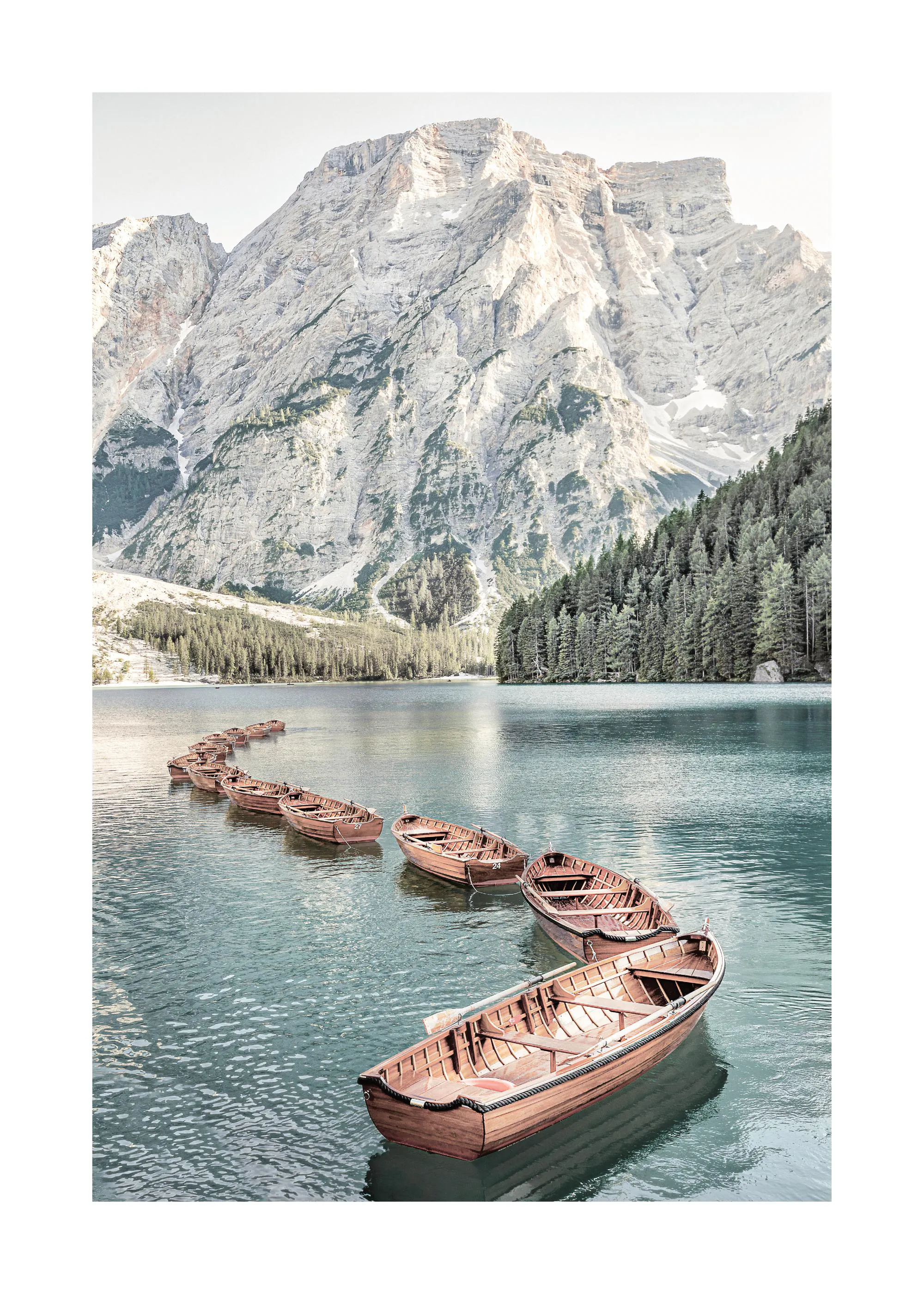 Poster con barche di legno ormeggiate in fila su un lago di montagna, circondato da pini e cime rocciose.