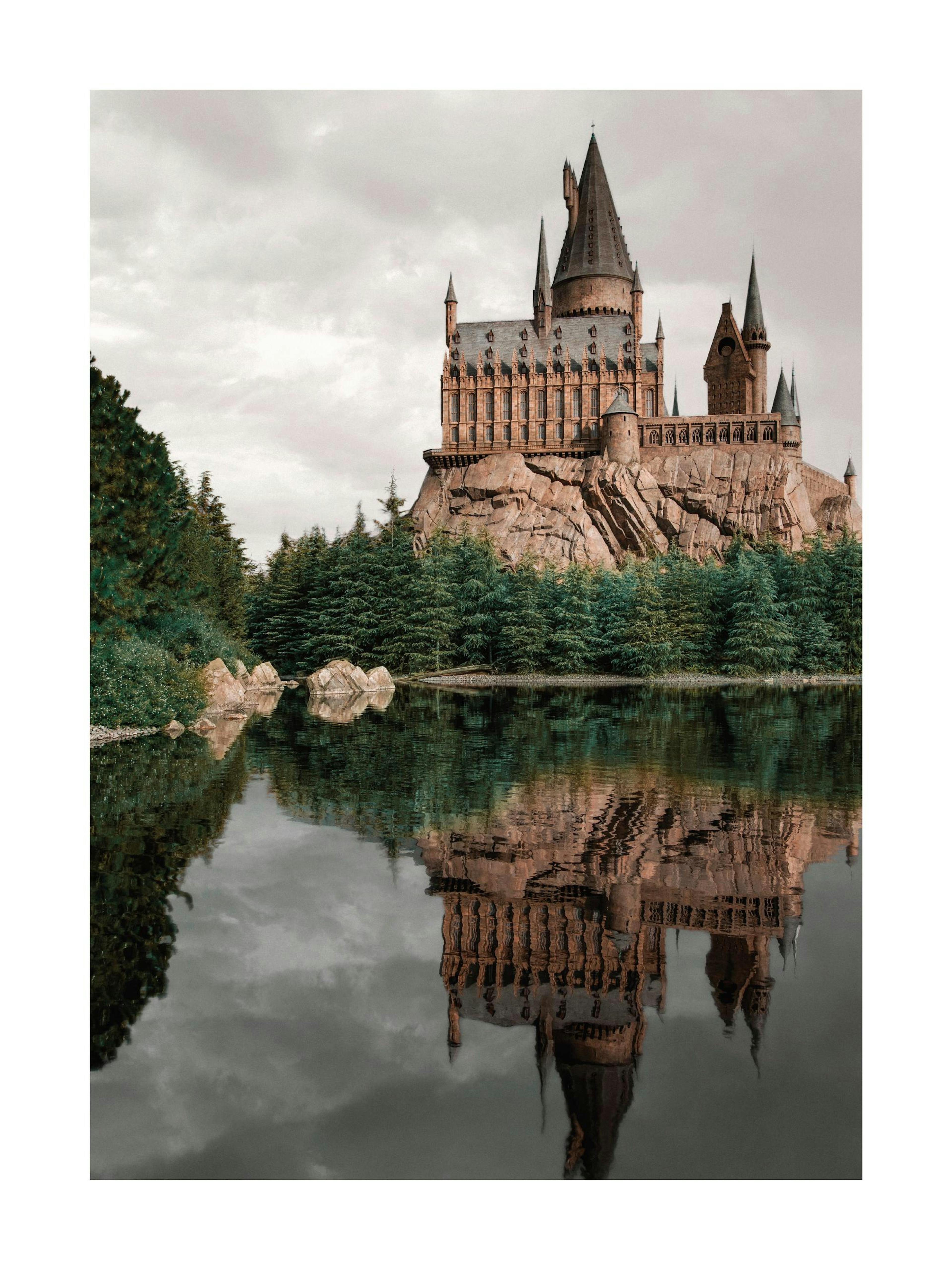 Un póster del castillo de Hogwarts en un acantilado, rodeado de árboles, con su reflejo en el agua.