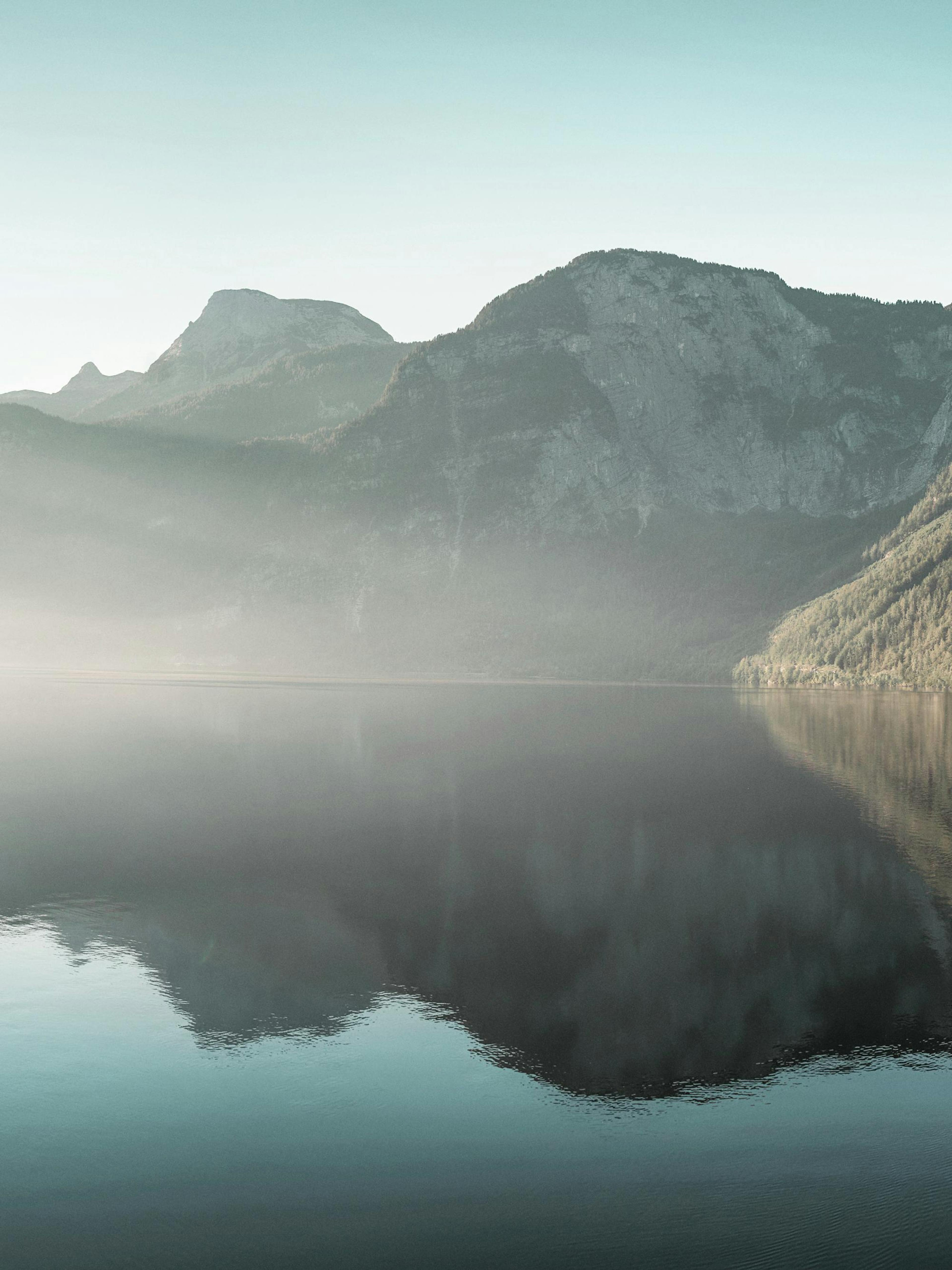 Poster eines Bergsees mit spiegelnder Wasseroberfläche und dunstigen Berghängen unter hellem Himmel.