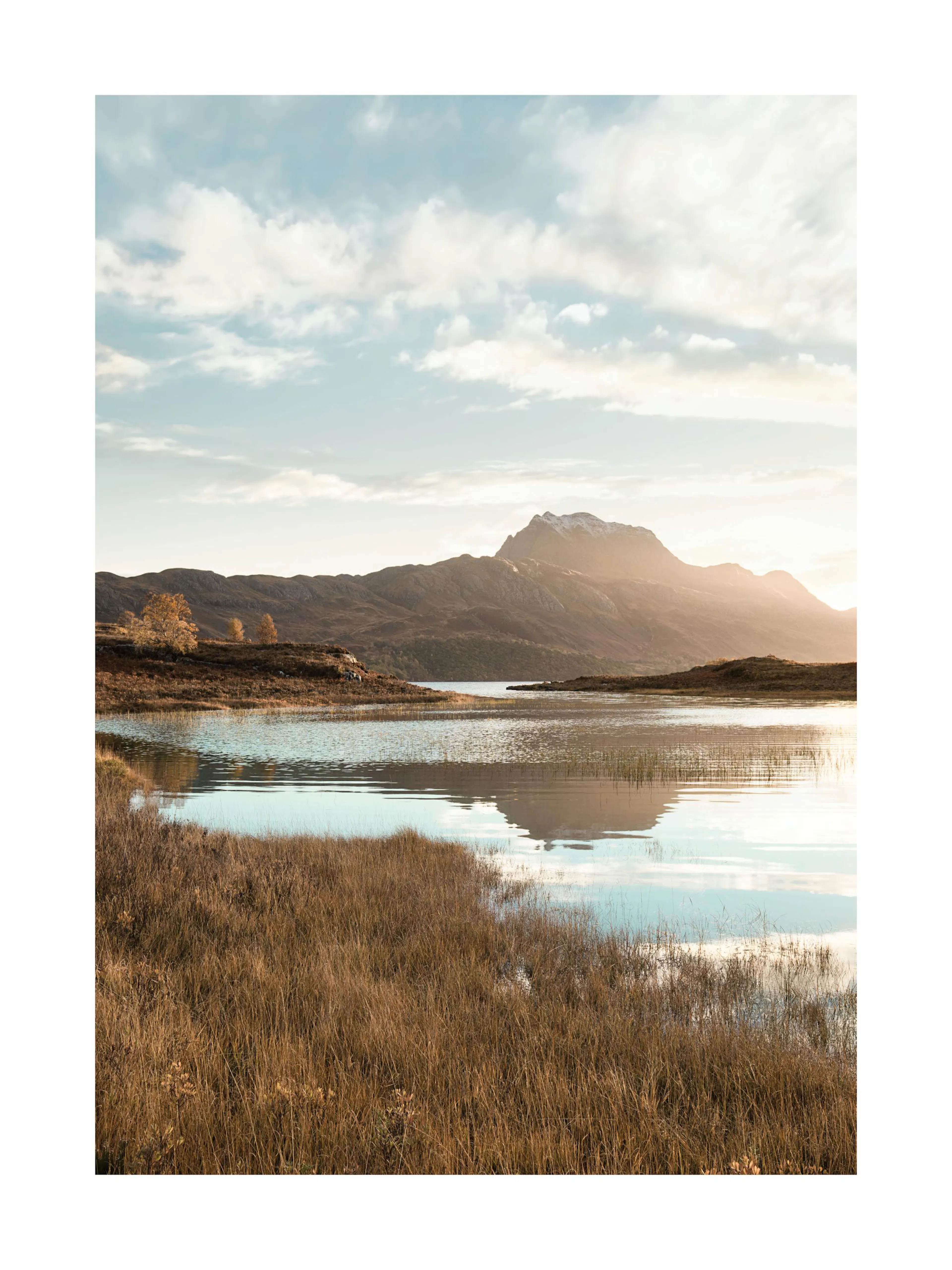 Poster con un lago tranquillo e montagne sullo sfondo, erba secca in primo piano e cielo nuvoloso al tramonto.