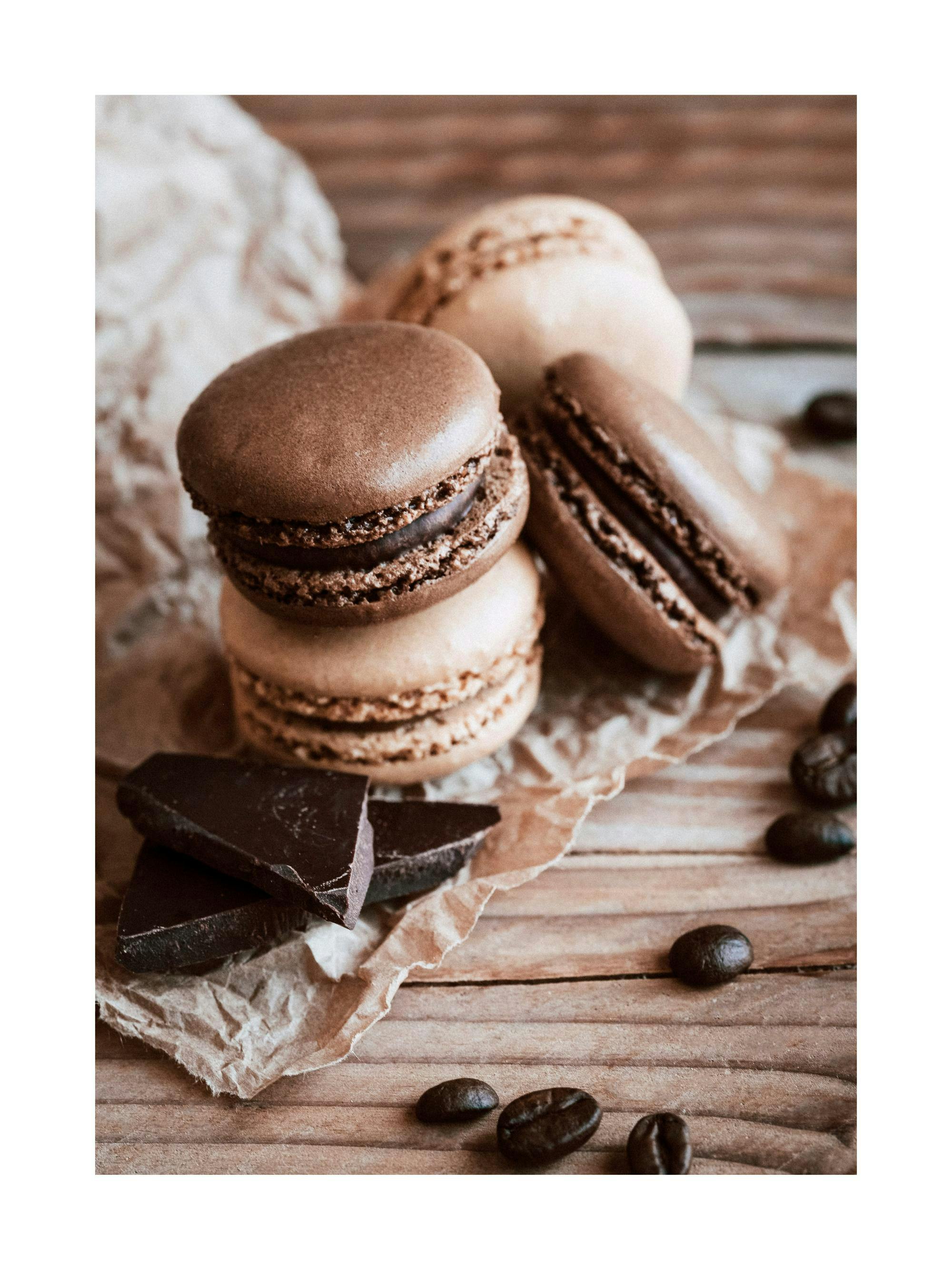 Poster de macarons au chocolat et à la vanille, grains de café et morceaux de chocolat sur bois rustique.