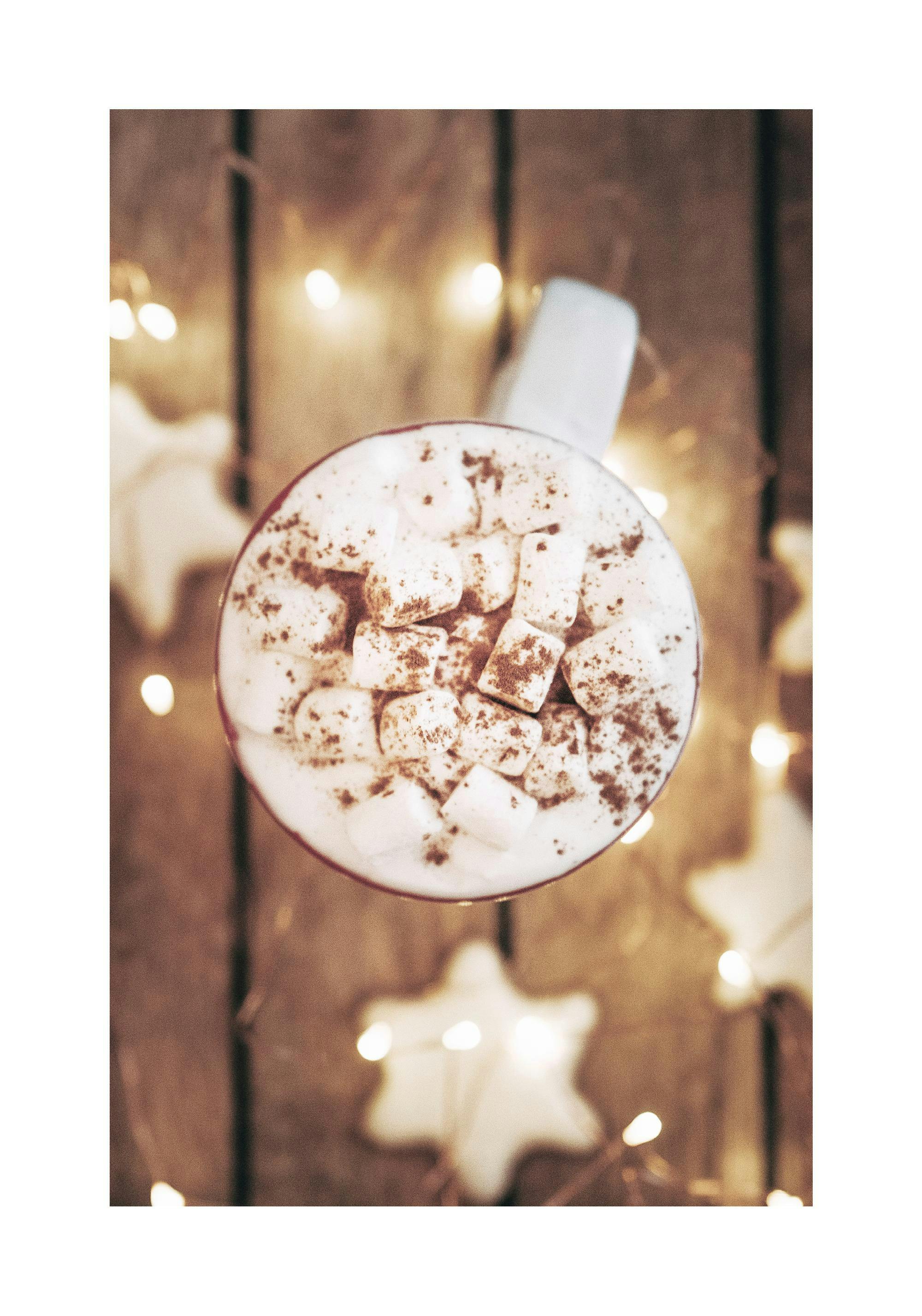 A poster featuring an overhead view of hot chocolate with marshmallows and cocoa powder, surrounded by blurred string lights and
