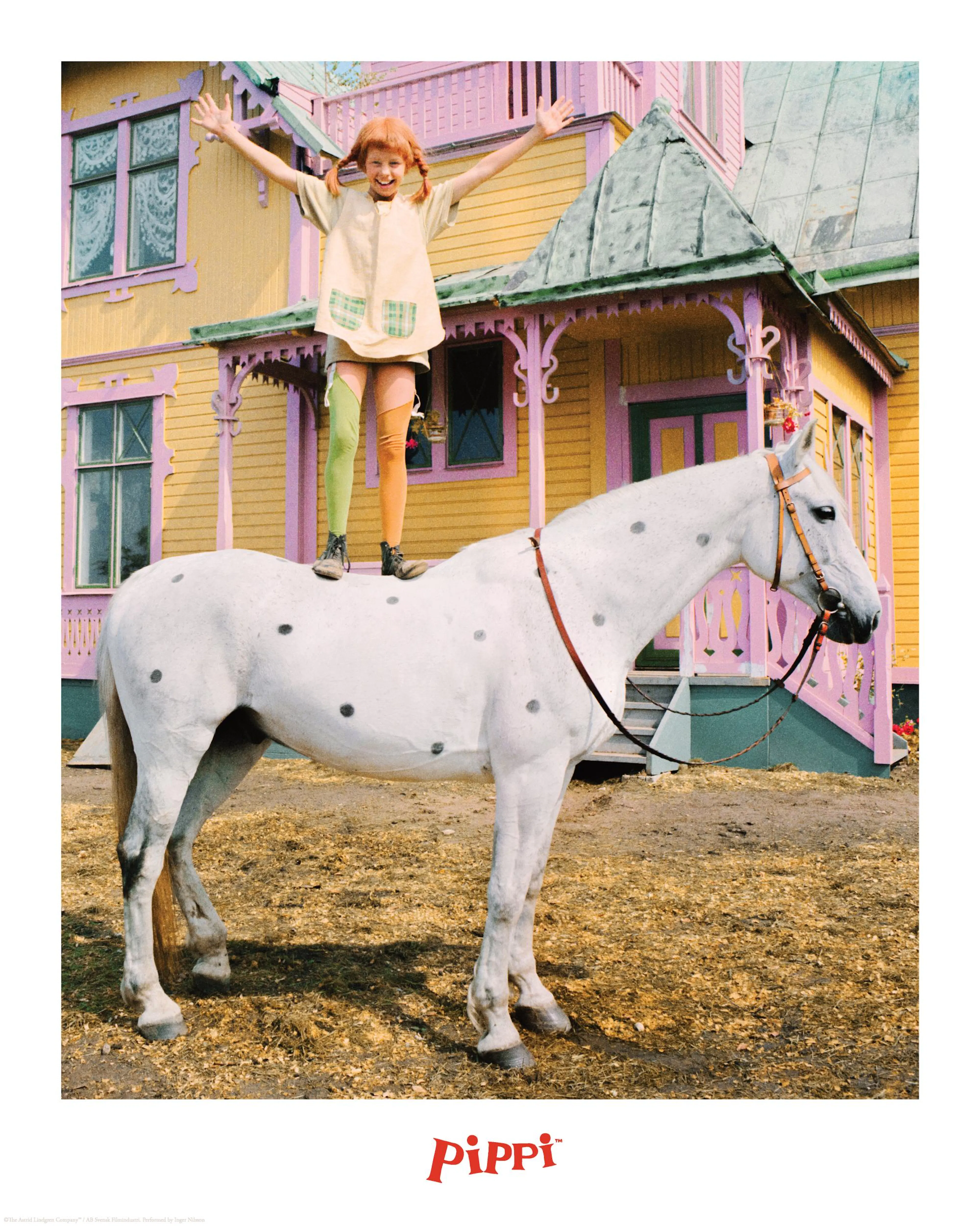Poster Pippi Långstrump debout sur un cheval blanc à pois noirs devant sa maison jaune et rose.