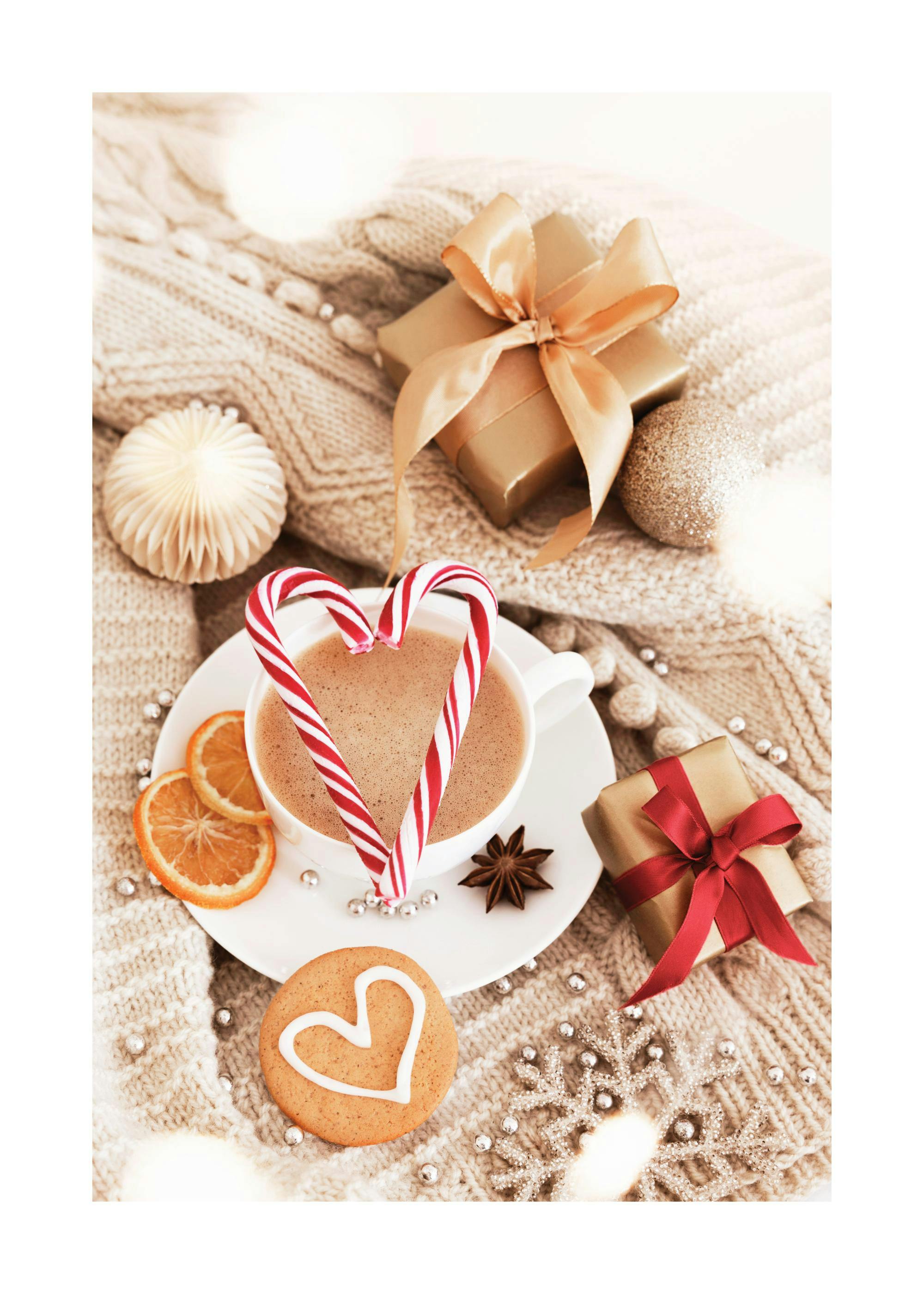 A cozy holiday poster of a hot drink with heart-shaped candy canes, gifts, a gingerbread cookie, and ornaments on a knitted blan