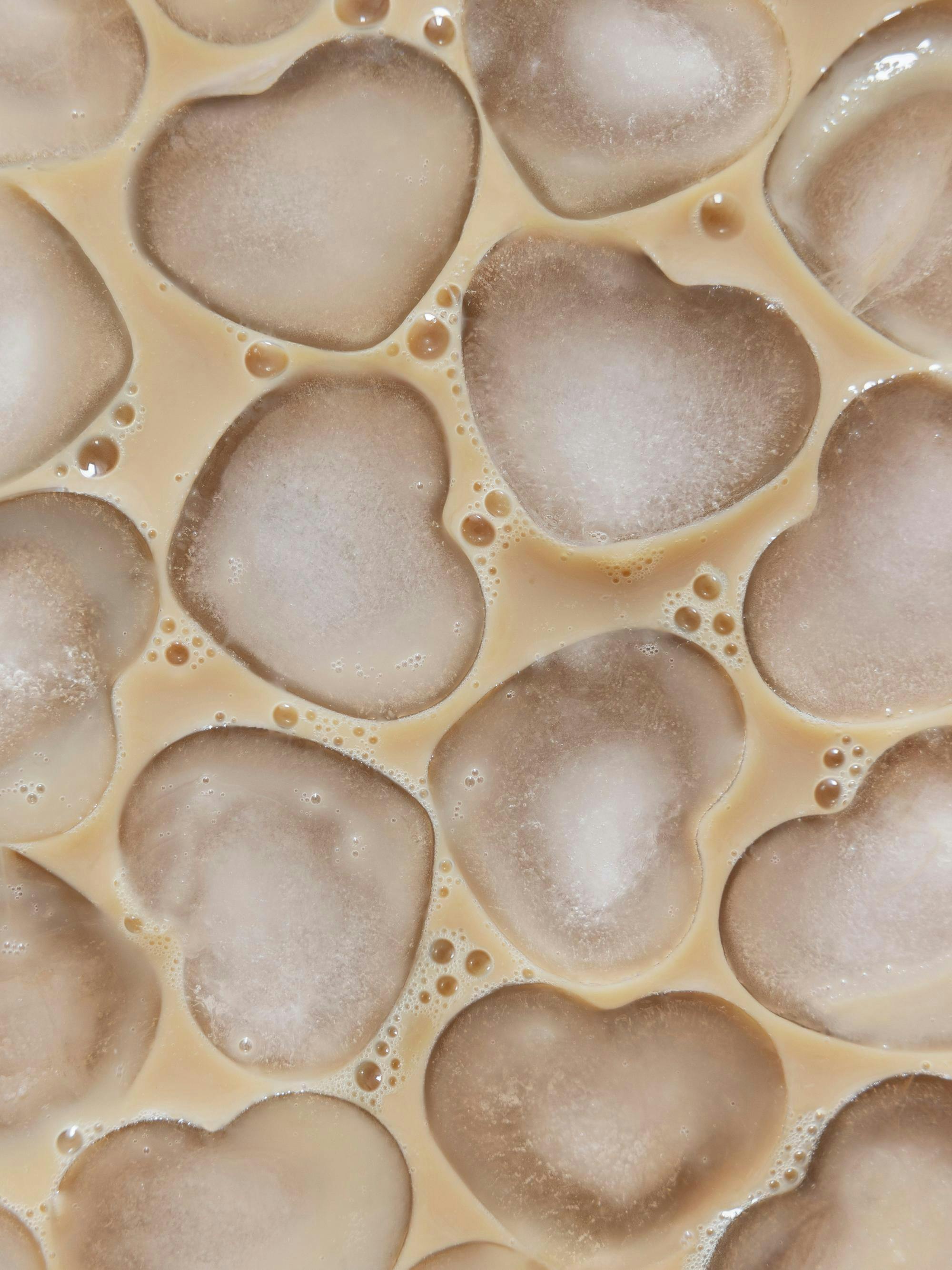 Póster de cubitos de hielo con forma de corazón flotando en un líquido cremoso color café con leche, con burbujas.