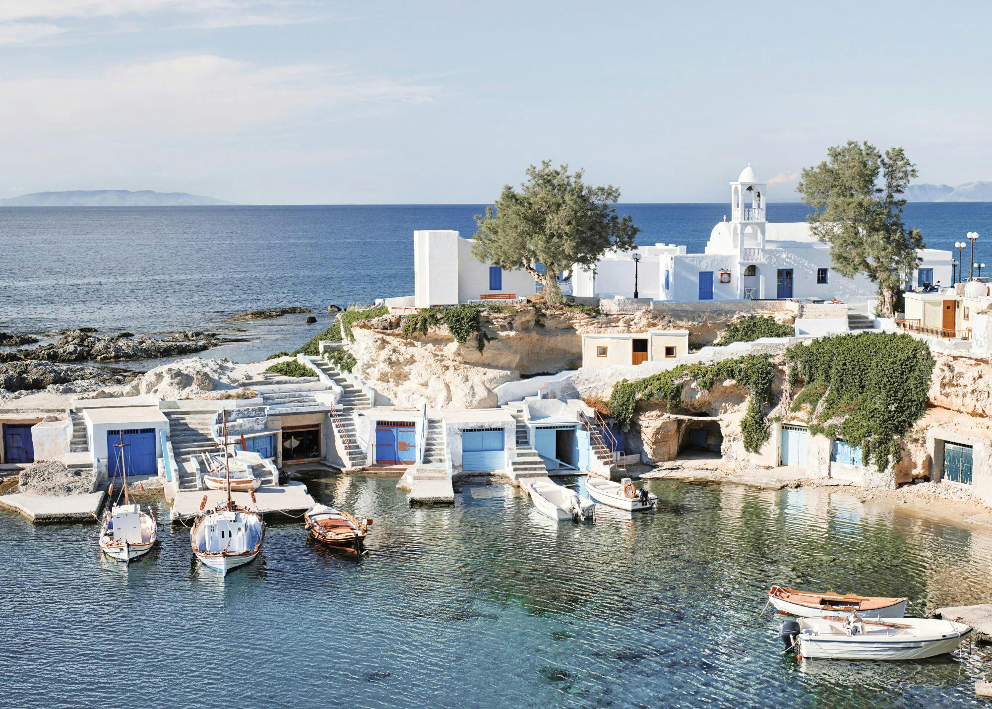 A poster of a secluded Greek fishing village with white buildings, blue doors, and boats in clear turquoise water.