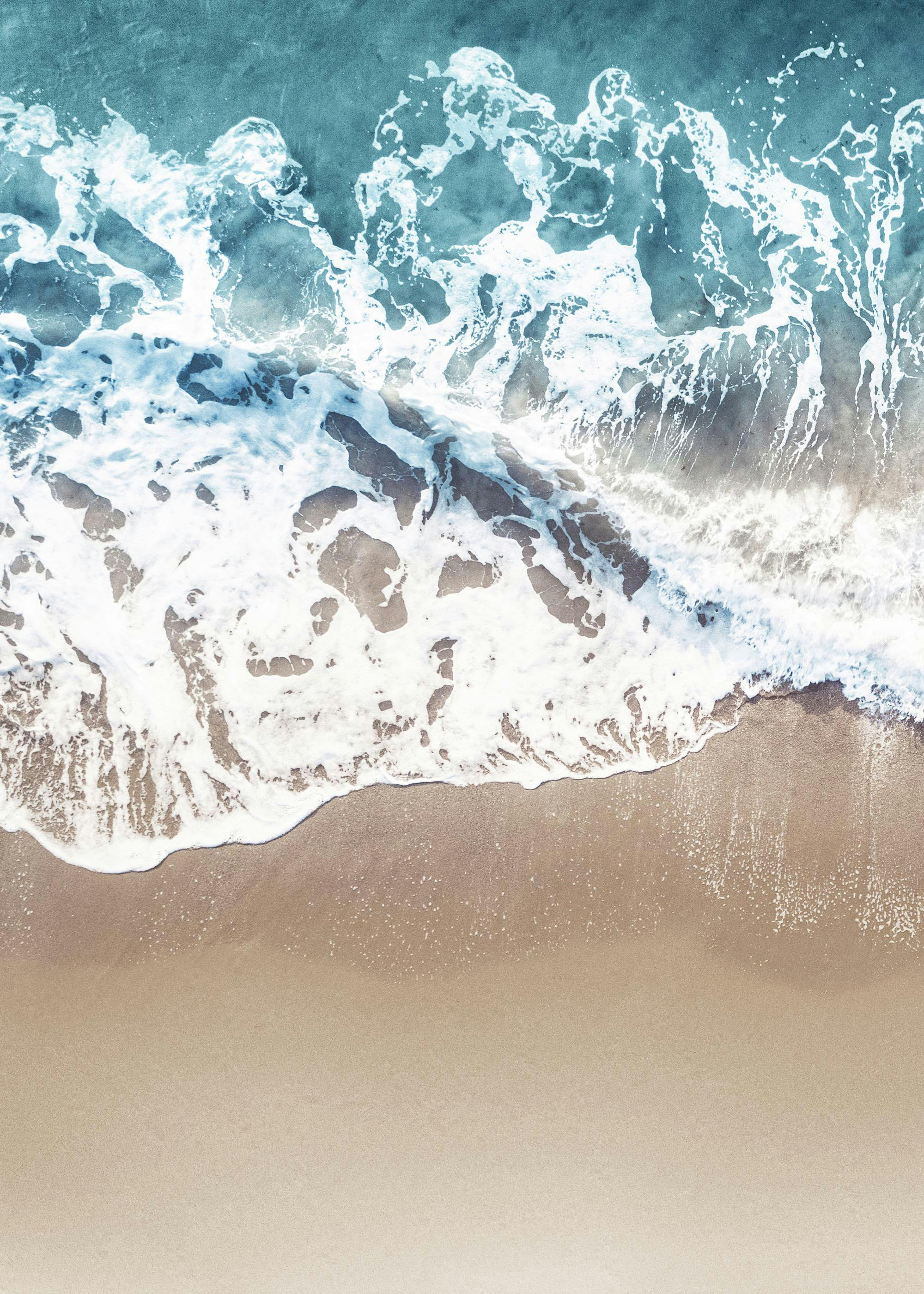 A poster featuring an aerial view of a vibrant blue ocean wave crashing onto a sandy beach.