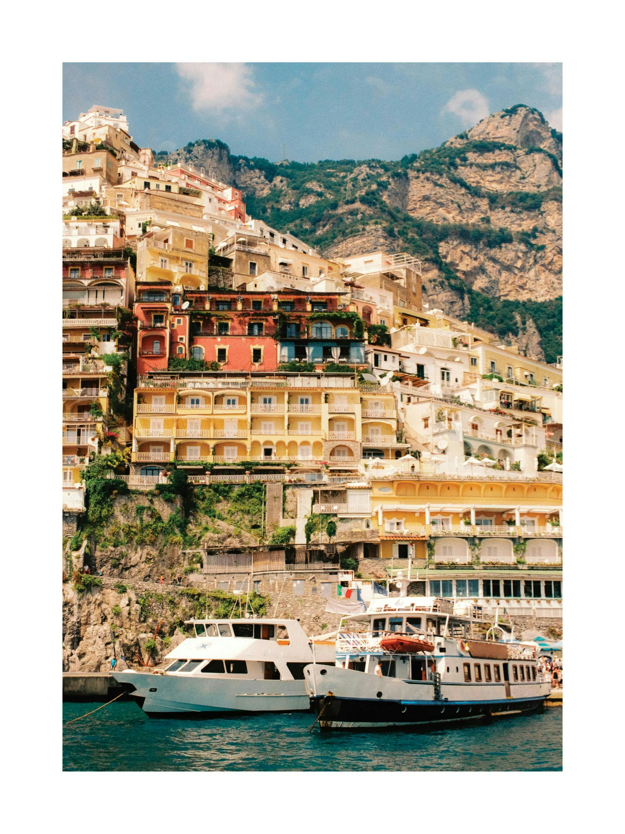 Un poster représentant des maisons colorées sur une colline rocheuse, avec des bateaux sur leau turquoise au premier plan.