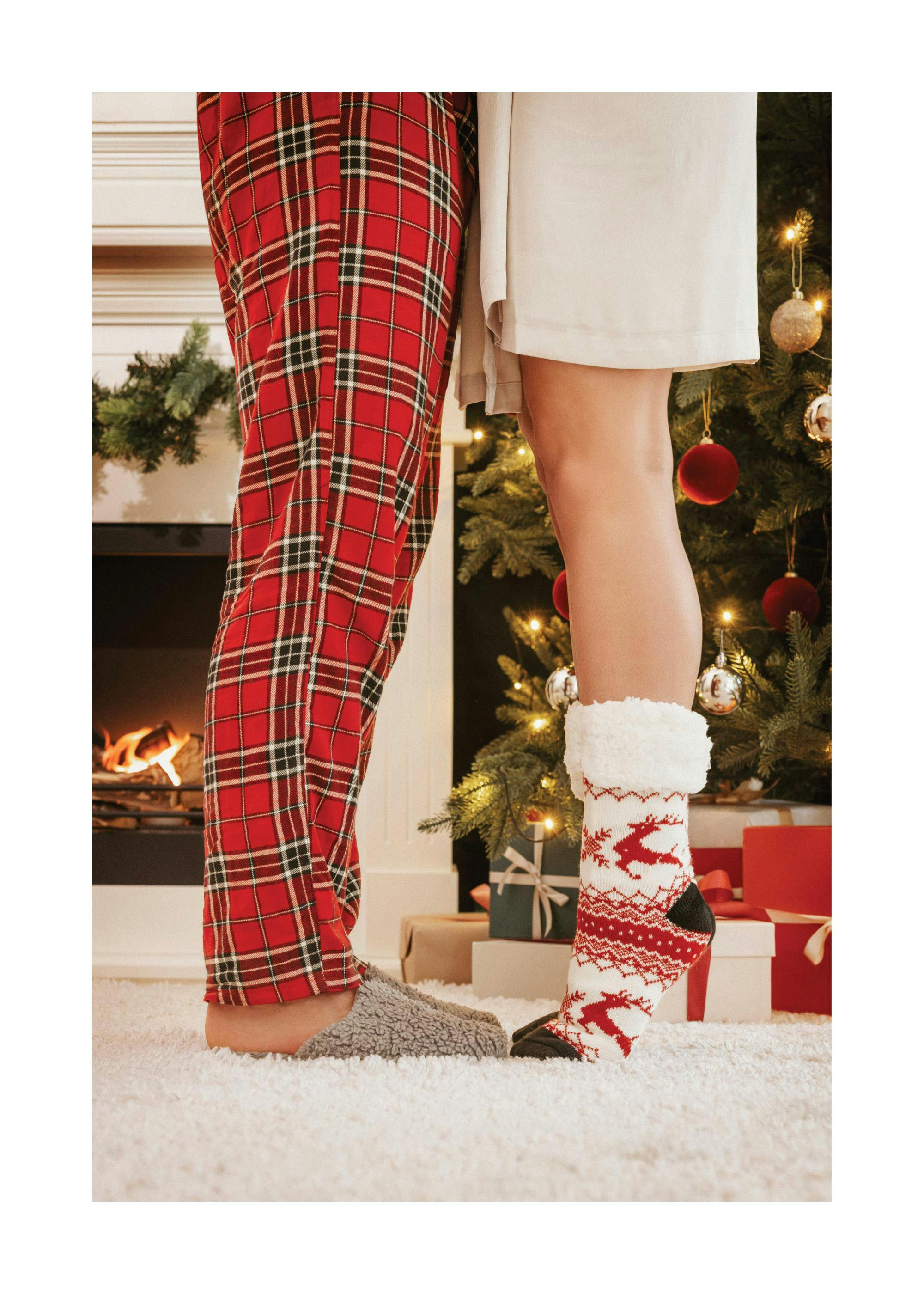 A poster showing two people standing by a Christmas tree, one in red plaid pyjamas and the other in white fluffy reindeer socks.