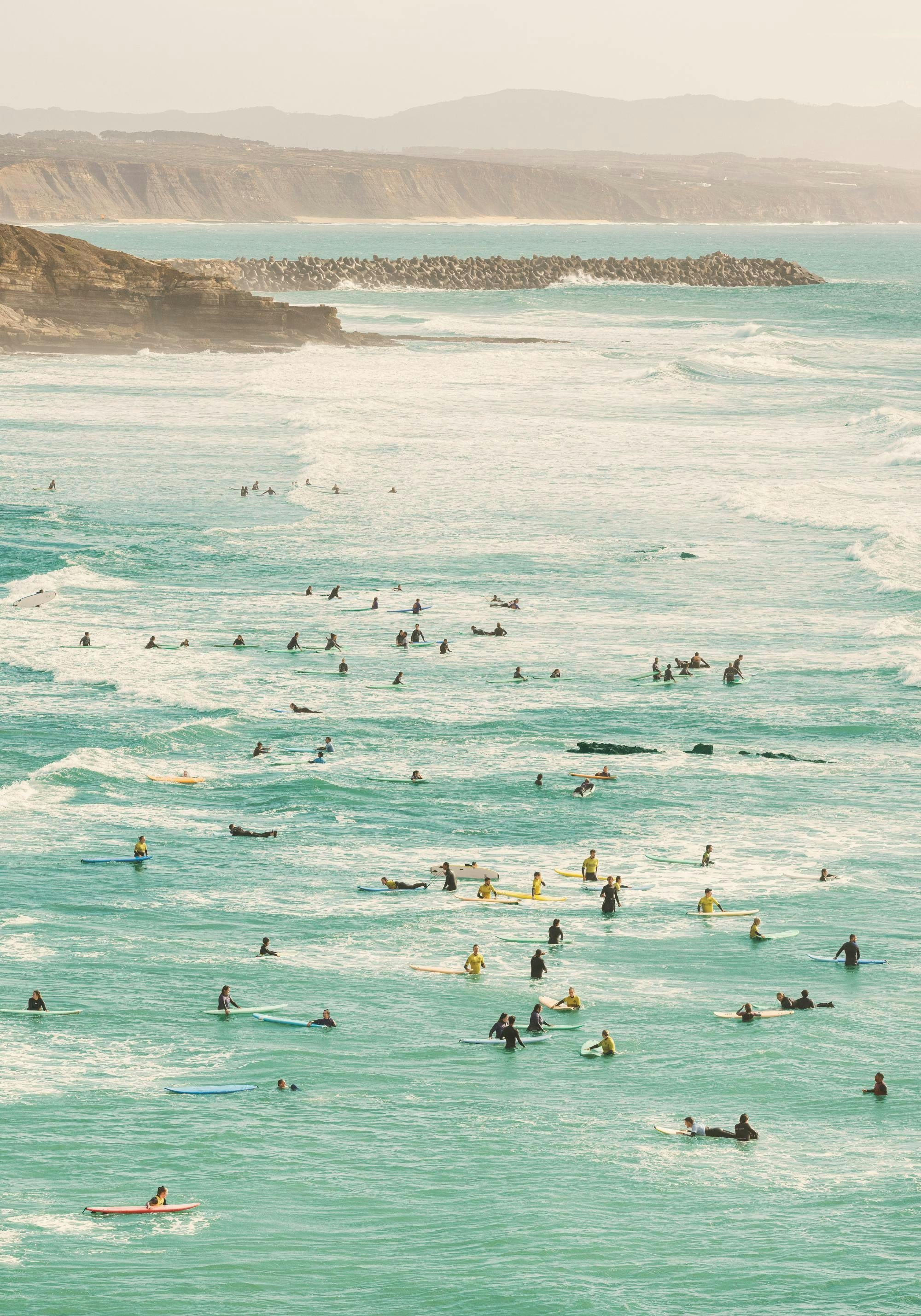 A poster of a surfing scene with many surfers floating on turquoise water near a rocky coastline.