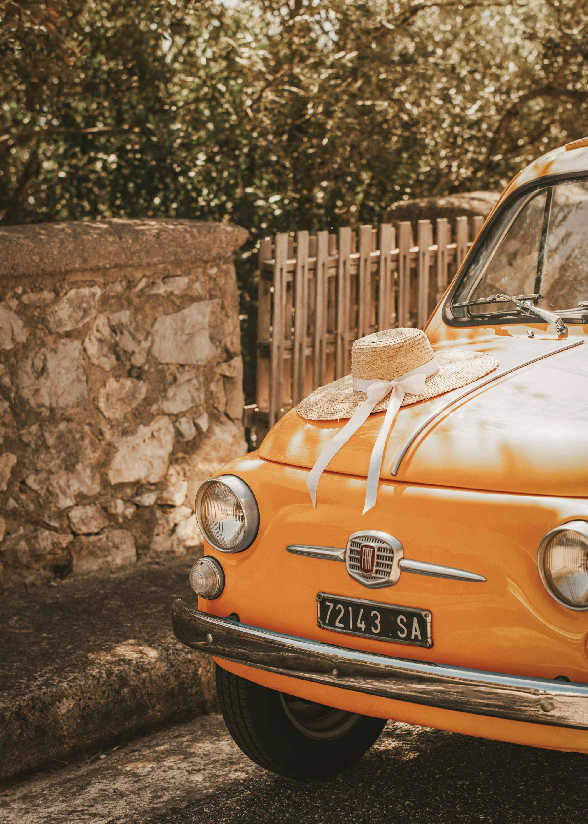 A poster featuring the front of a vintage orange Fiat car with a straw hat and white ribbon on the hood.