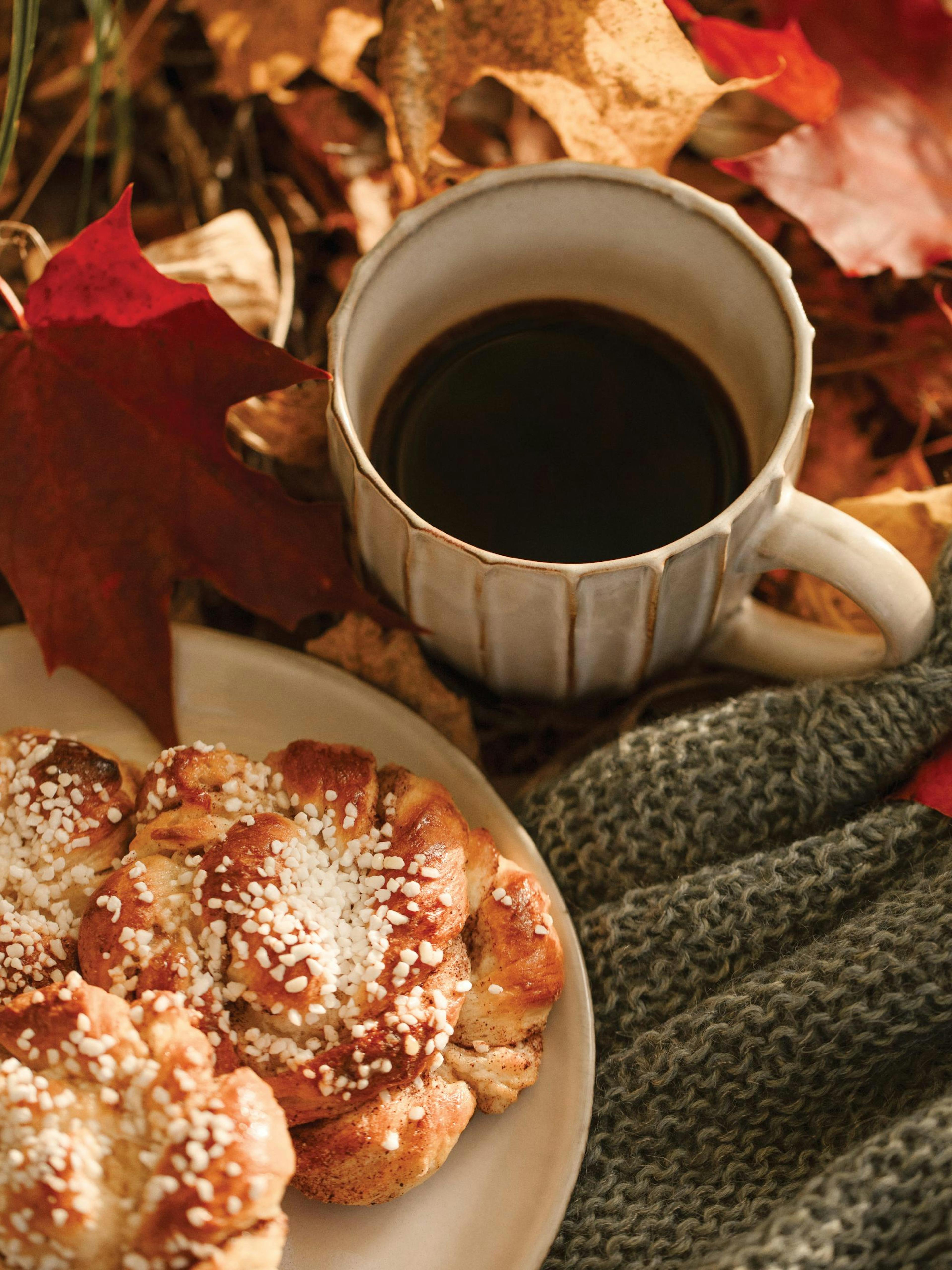 A poster featuring a mug of coffee, cinnamon buns, a grey knitted blanket, and autumn leaves.