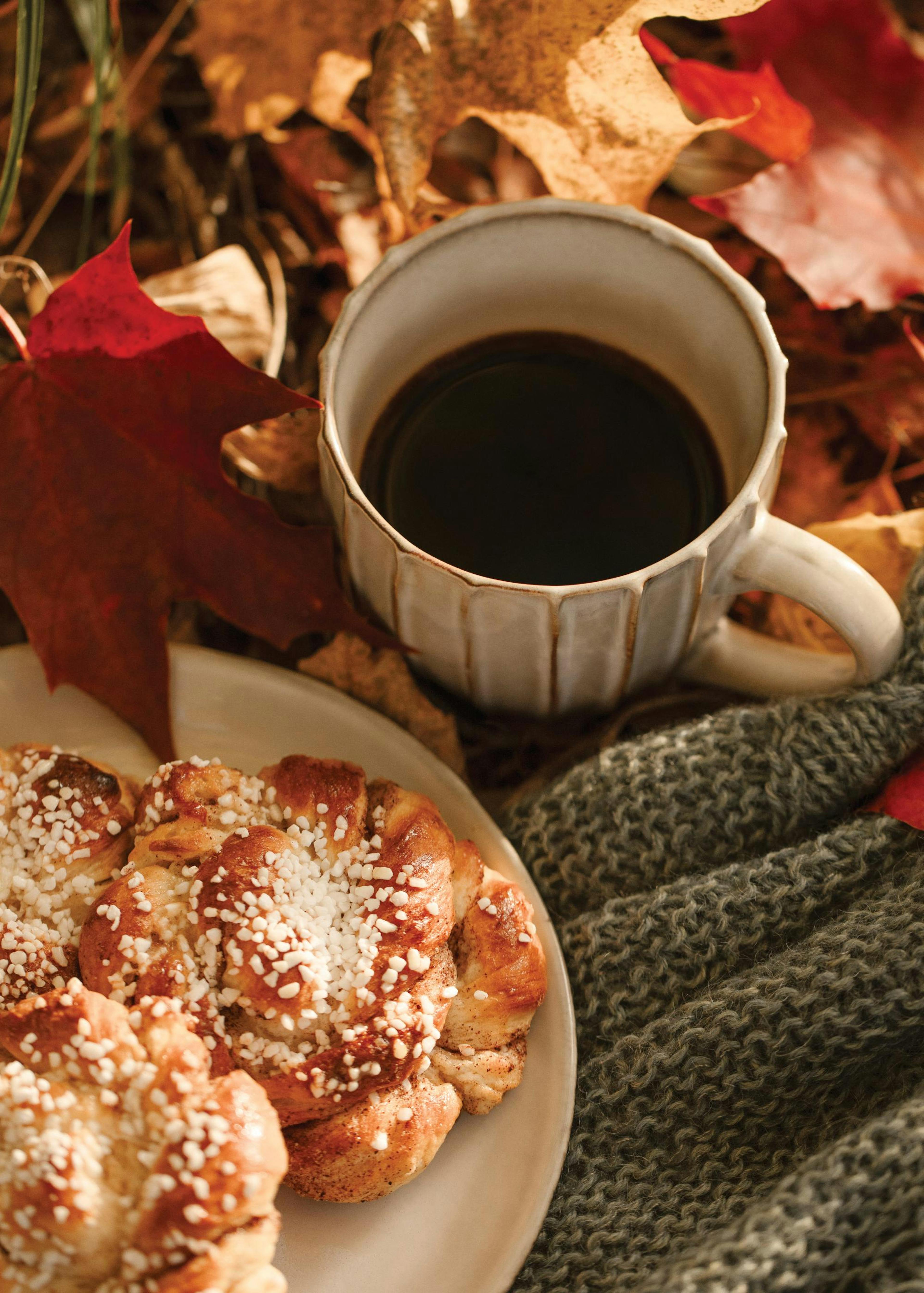 A poster featuring a mug of coffee, cinnamon buns, a grey knitted blanket, and autumn leaves.