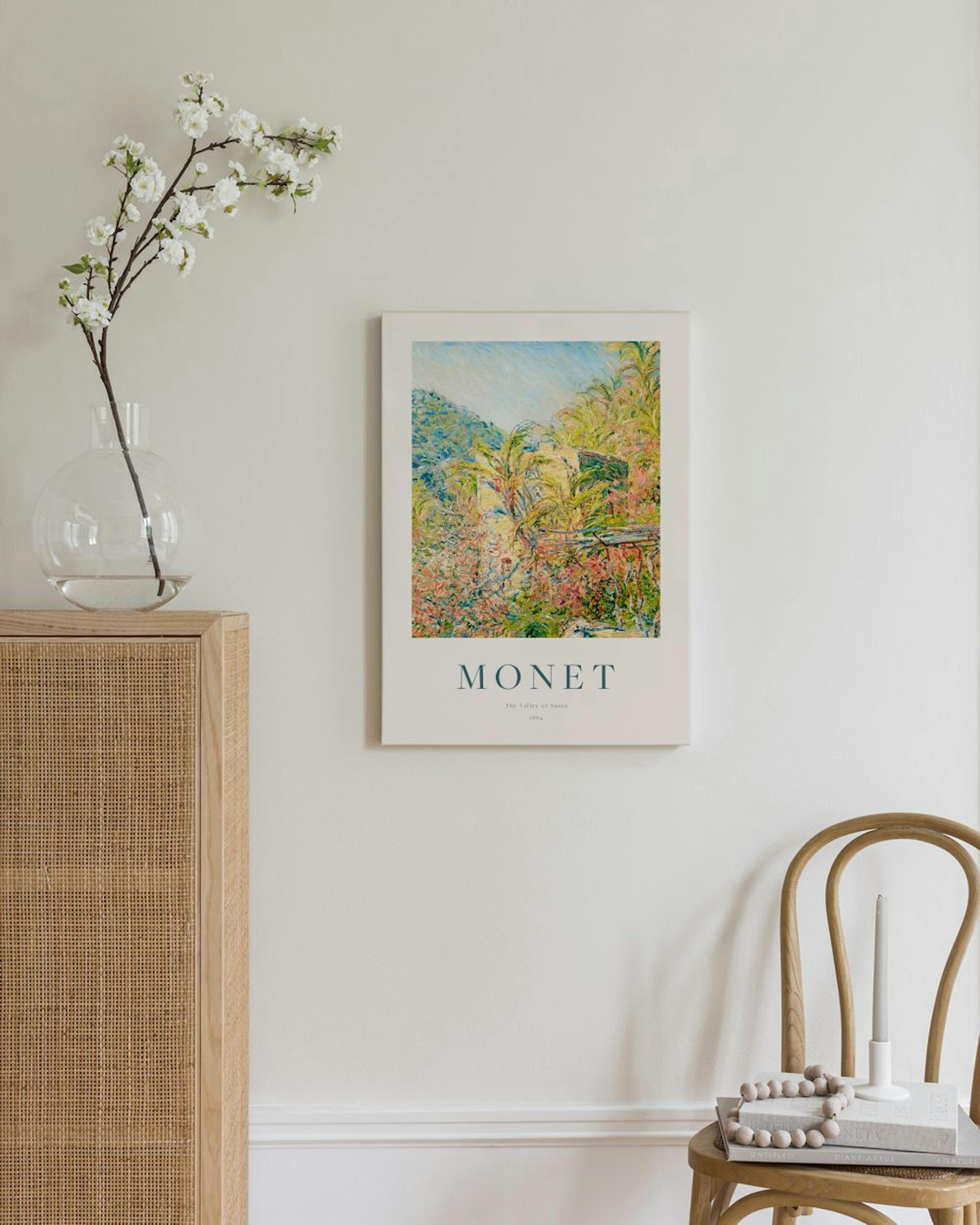 Monet-kanvaasi puutalon ja kukkivan pensaikon kuvalla ripustettuna olohuoneen seinälle.