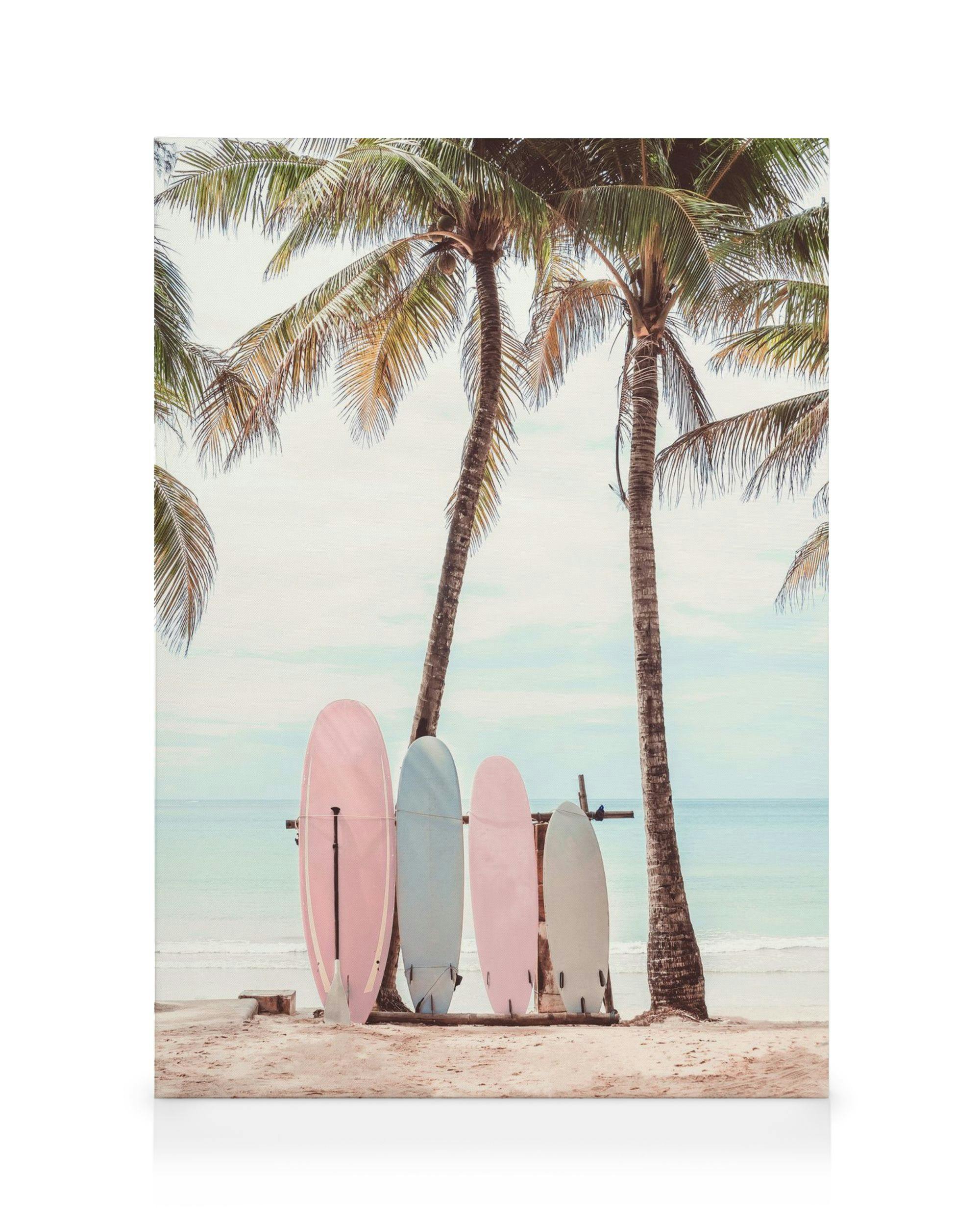 A canvas of pink, blue, and white surfboards on a sandy beach with palm trees and ocean in the background.