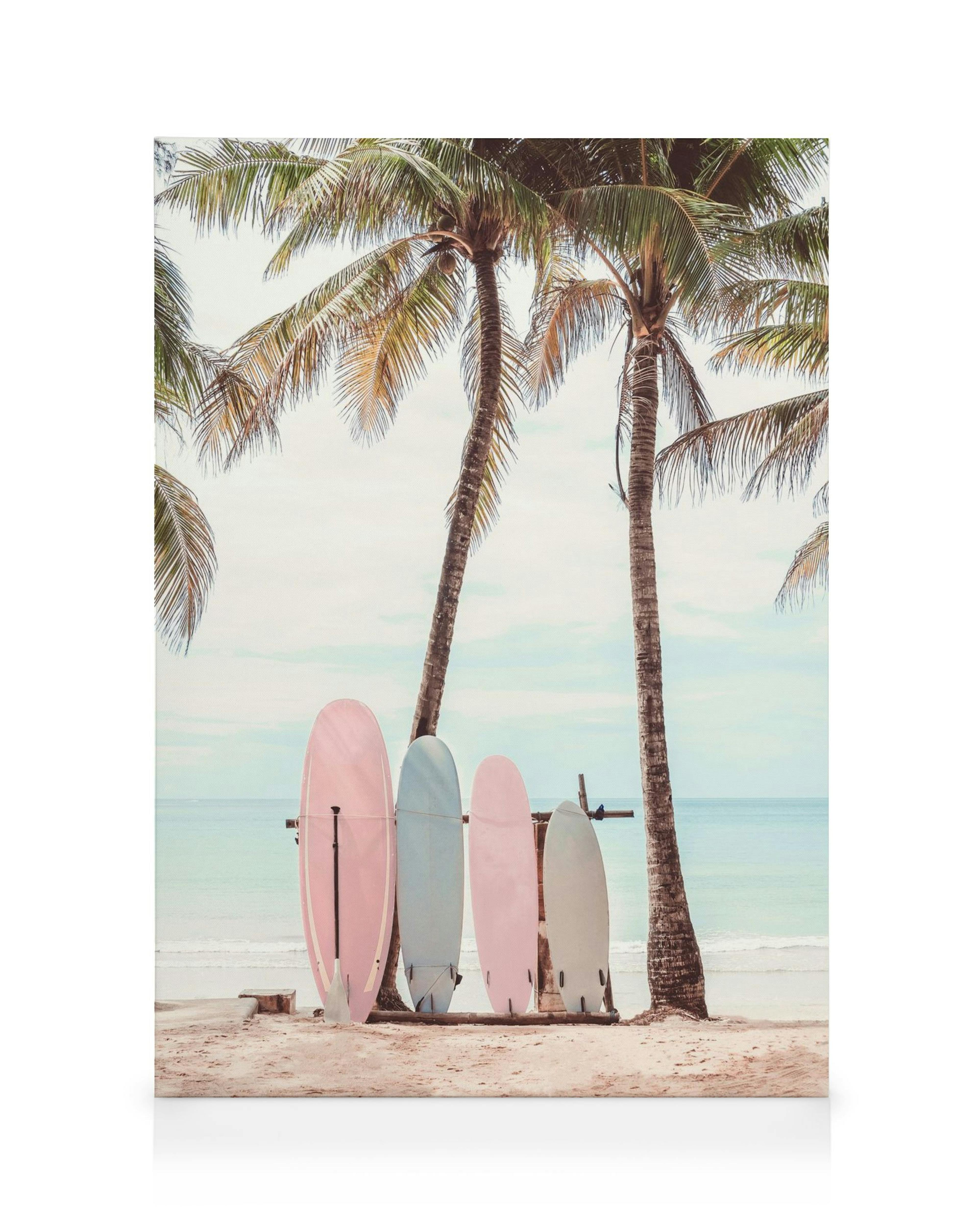 Lienzo de tablas de surf rosadas, azules y blancas en la playa, con palmeras y el océano de fondo.