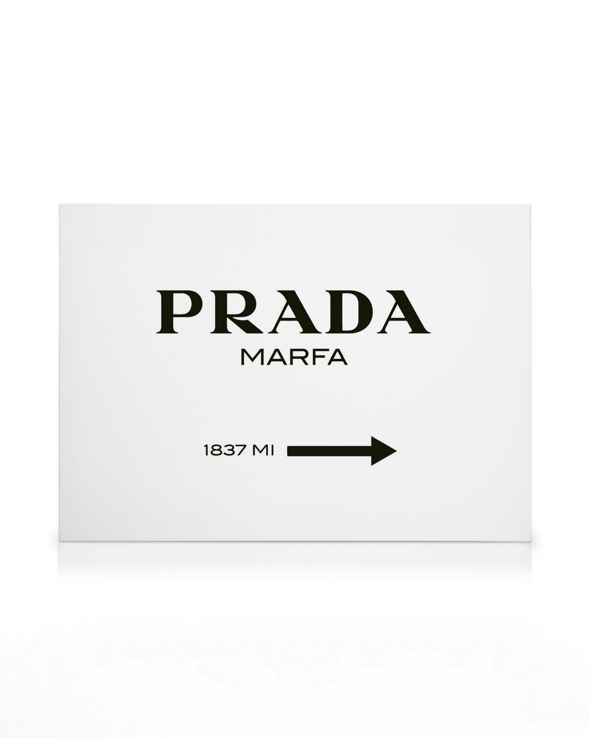 Obraz na płótnie z białym tłem, czarnym napisem Prada Marfa i strzałką z odległością 1837 mil.