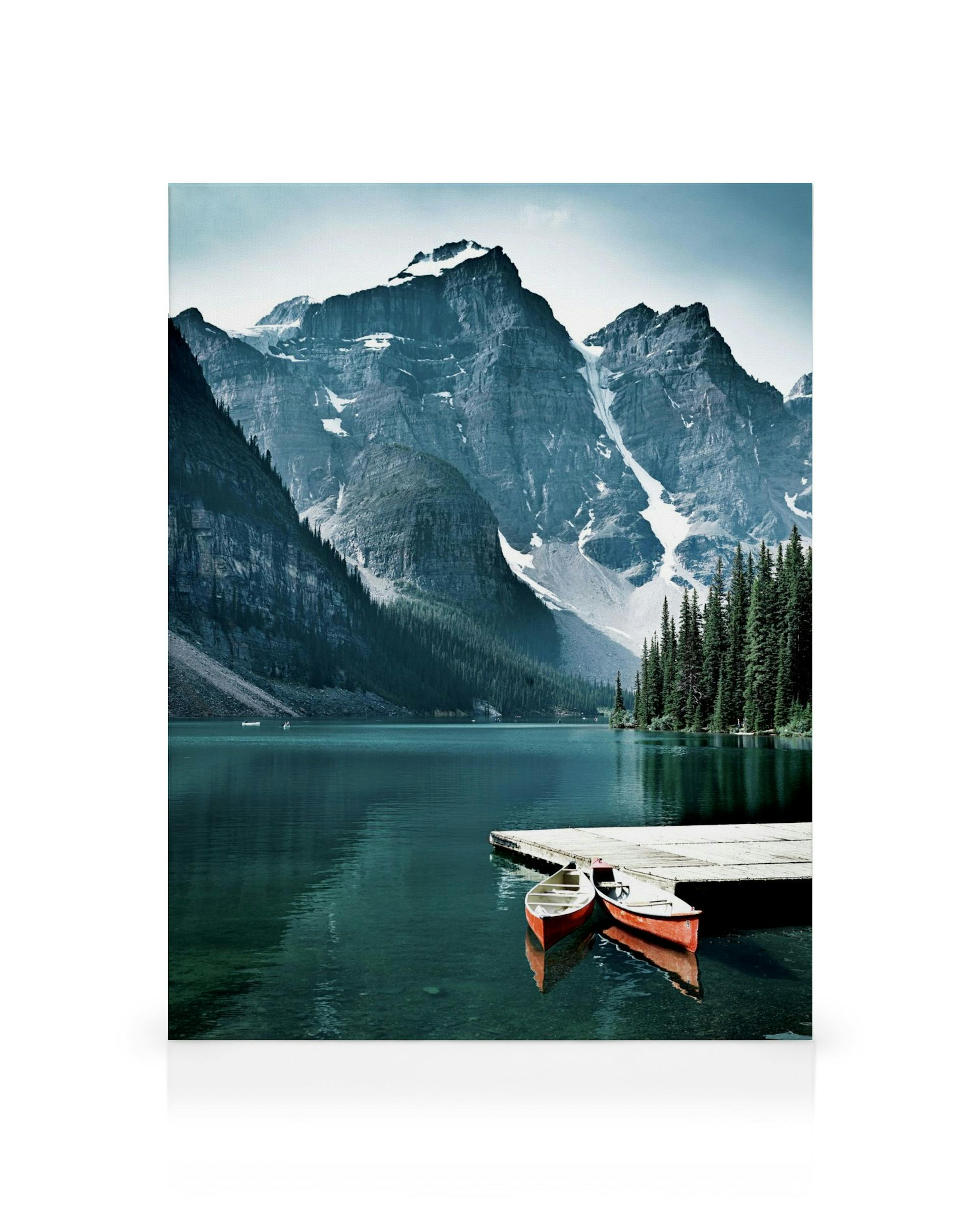 A canvas showing a serene blue lake with two red canoes by a dock, surrounded by majestic snow-capped mountains and evergreen tr