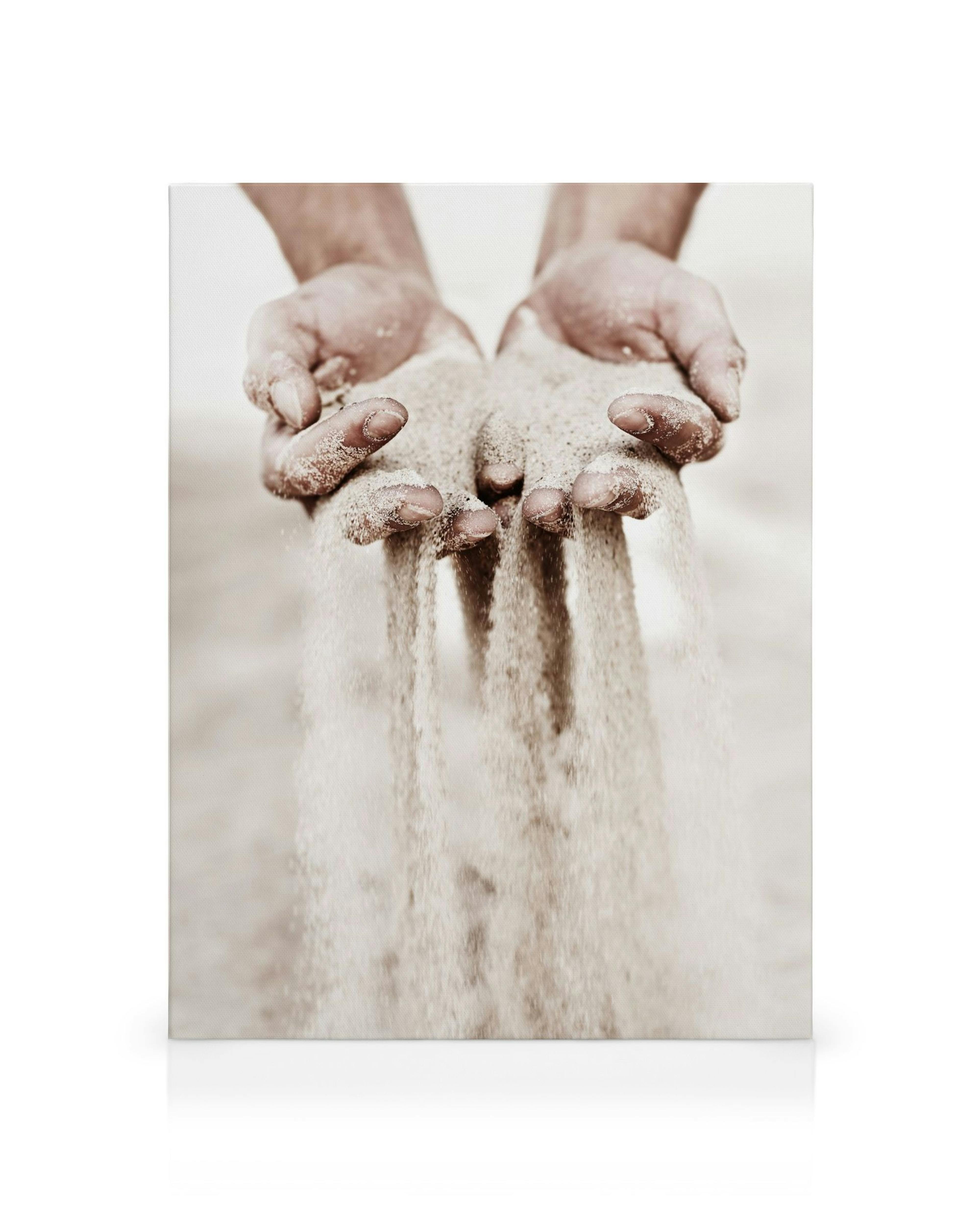 A canvas showing human hands holding sand, with grains of sand falling between the fingers in sepia tones.