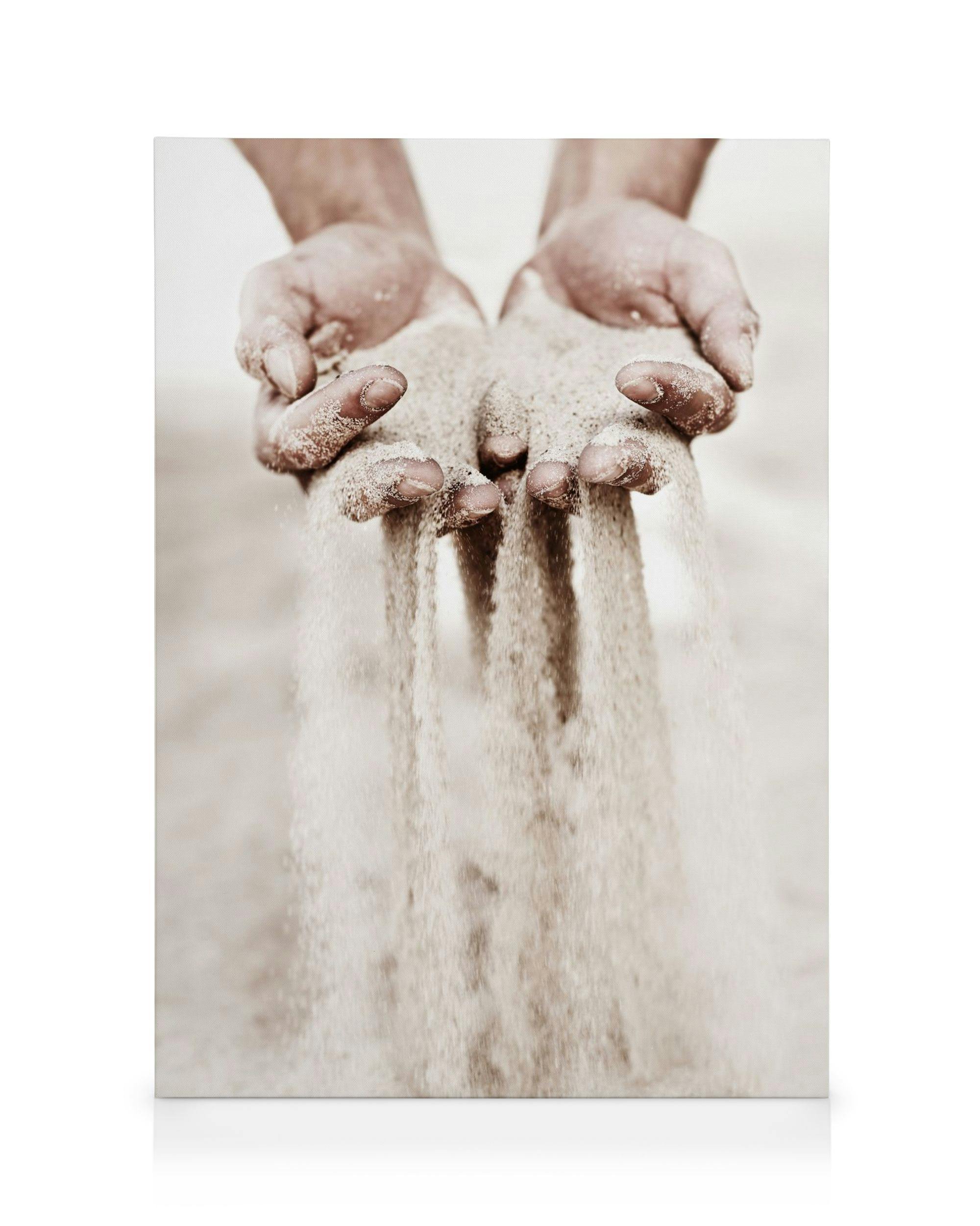 A sepia-toned canvas of hands holding sand as it trickles through the fingers.