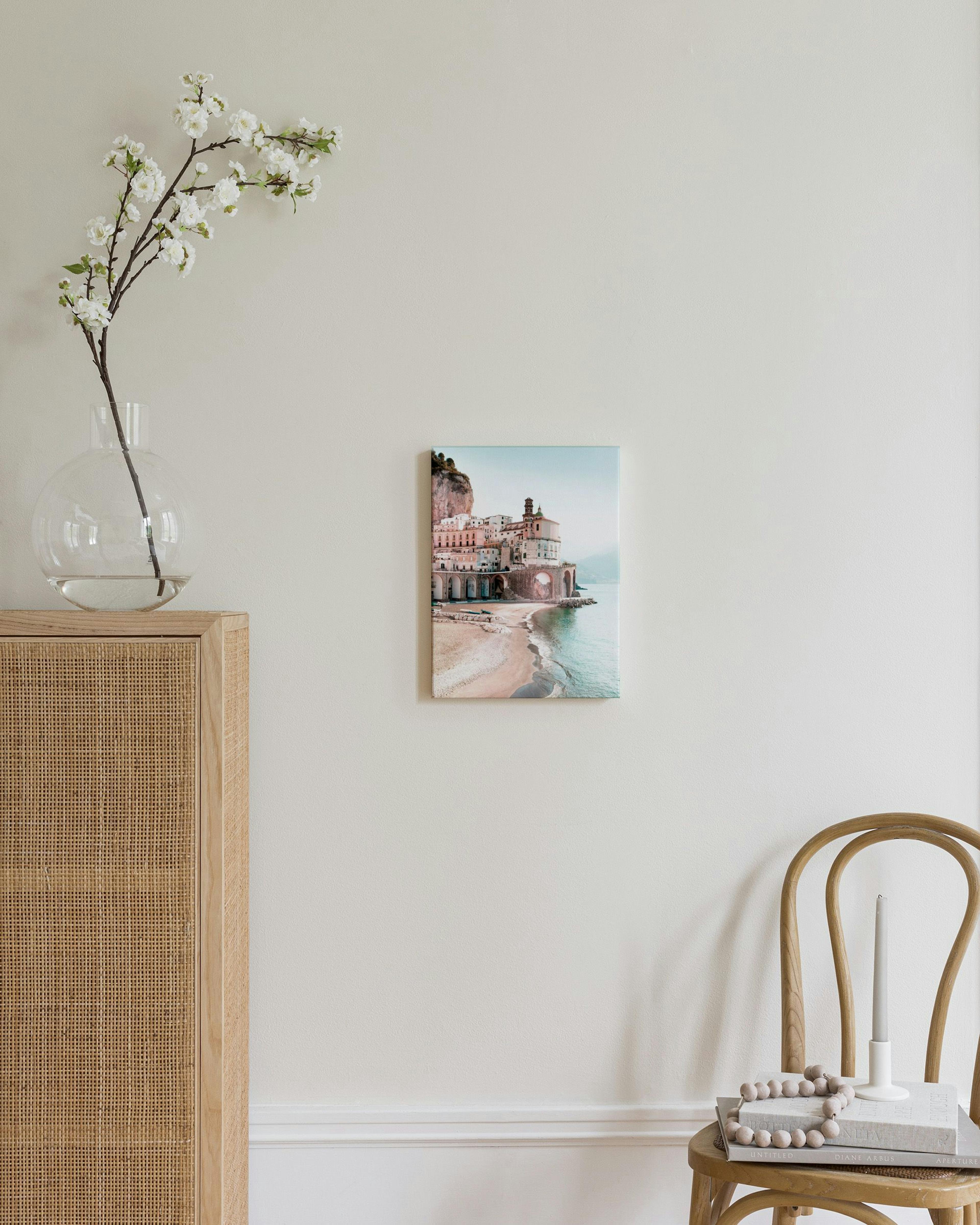 Leinwandbild mit Küstenstadt, Strand und Meer, hängt in einem modernen Wohnzimmer über einem Hocker.