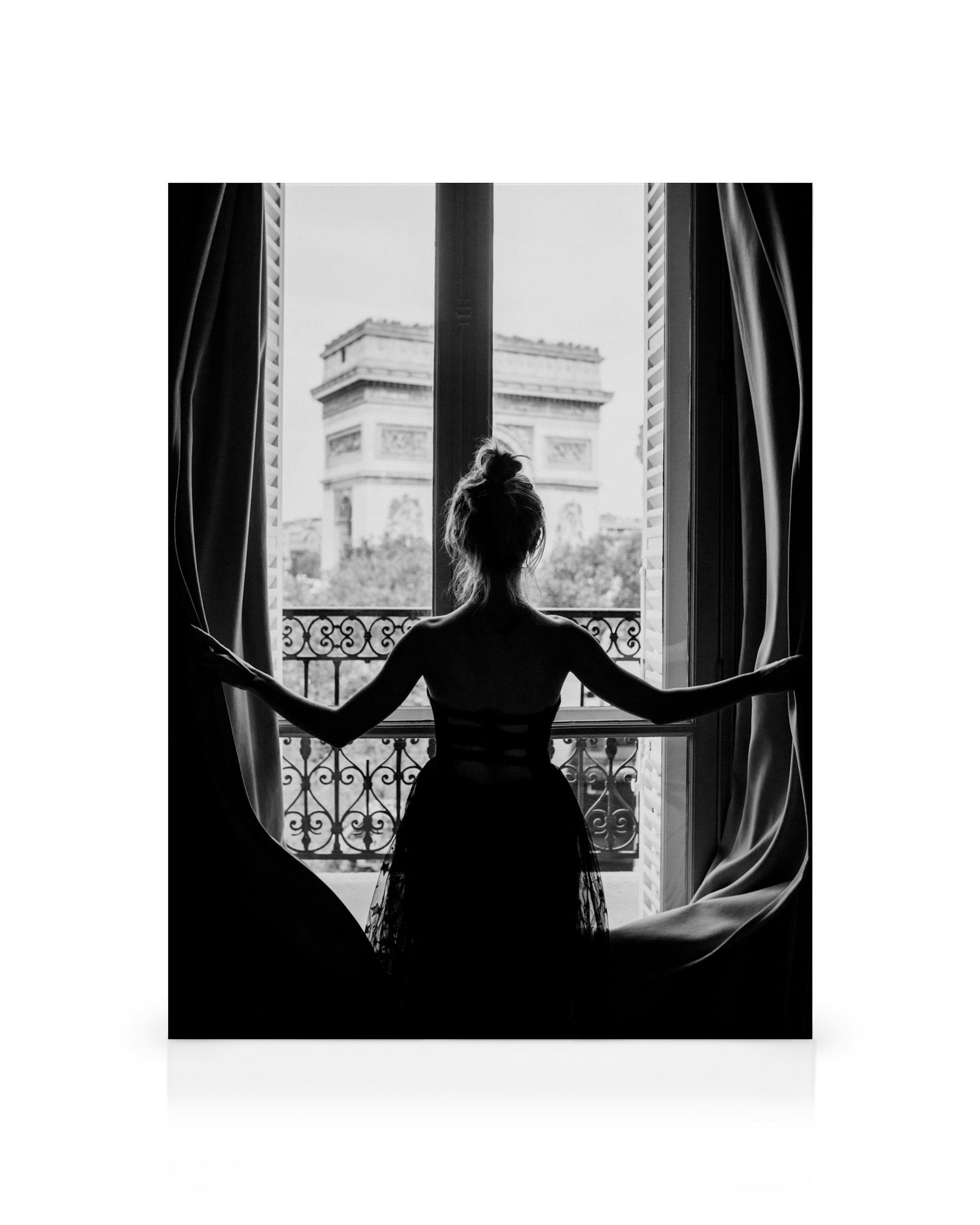 A black and white canvas of a woman silhouetted against a window, looking out at the Arc de Triomphe.
