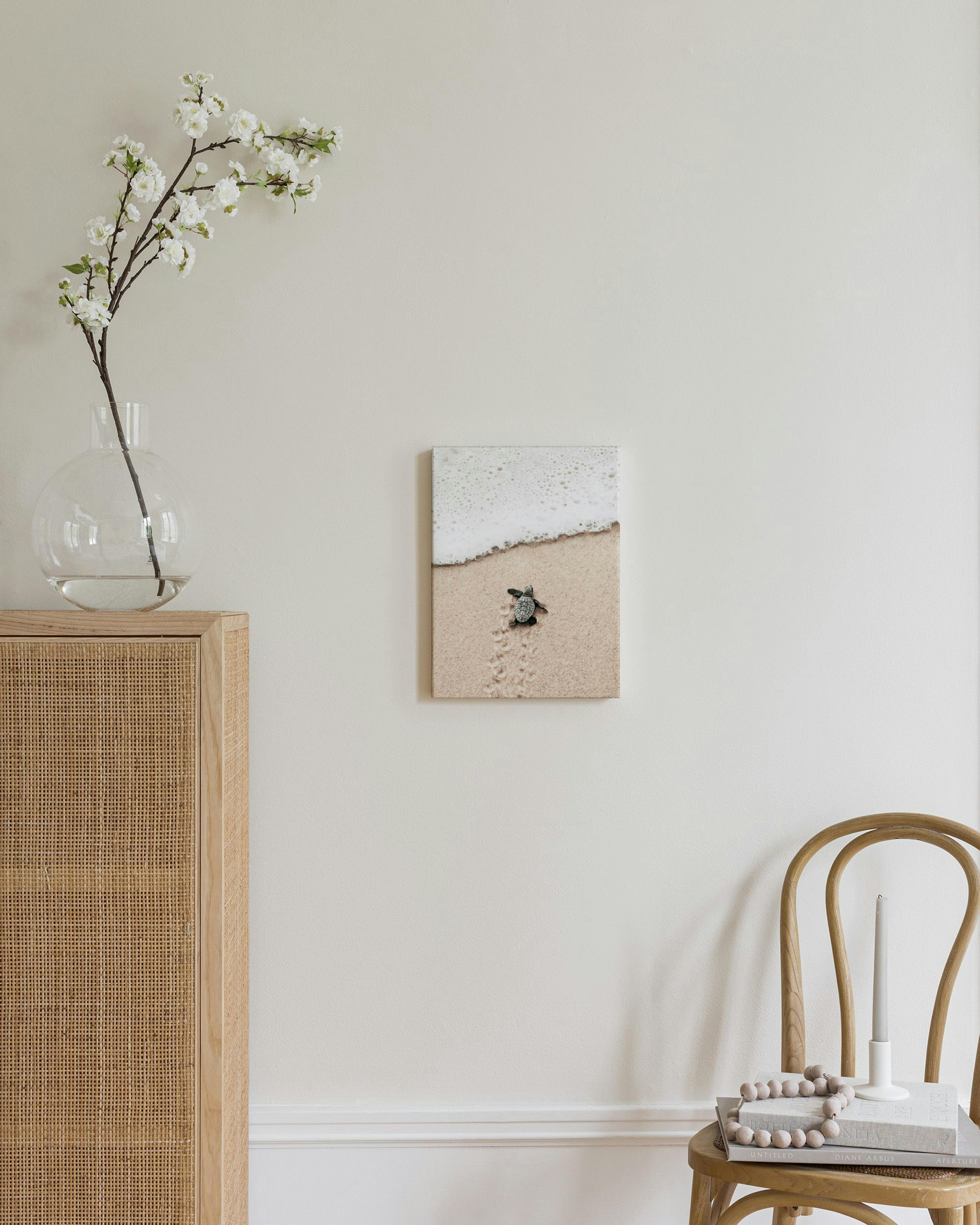 A print of a baby sea turtle walking on sand towards frothy ocean waves, displayed in a bright modern room.
