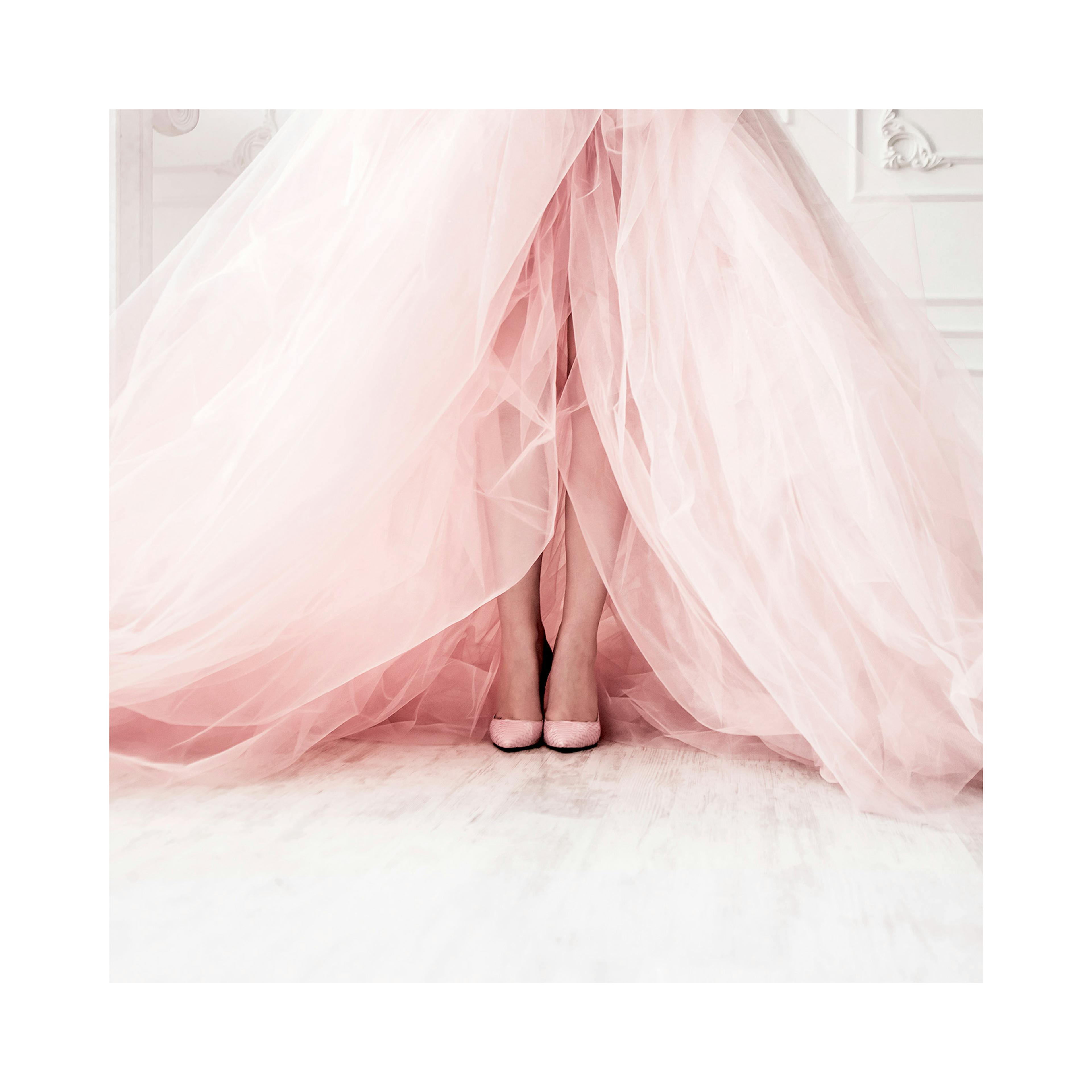 A poster featuring a persons feet and legs, partially covered by flowing light pink sheer fabric, against a white floor.