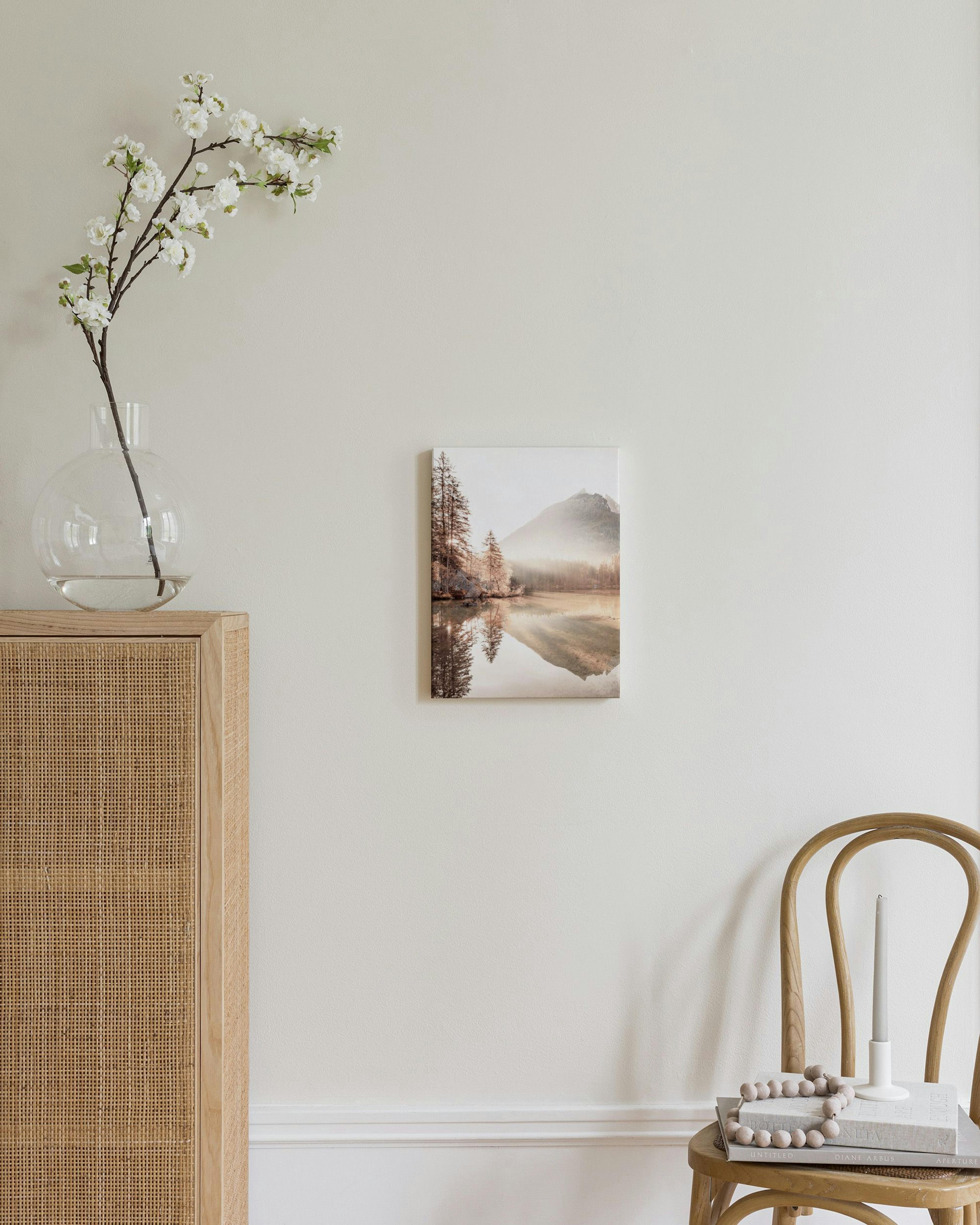 Canvas van een mistig berglandschap met weerspiegeling in een meer, hangend boven een houten dressoir.
