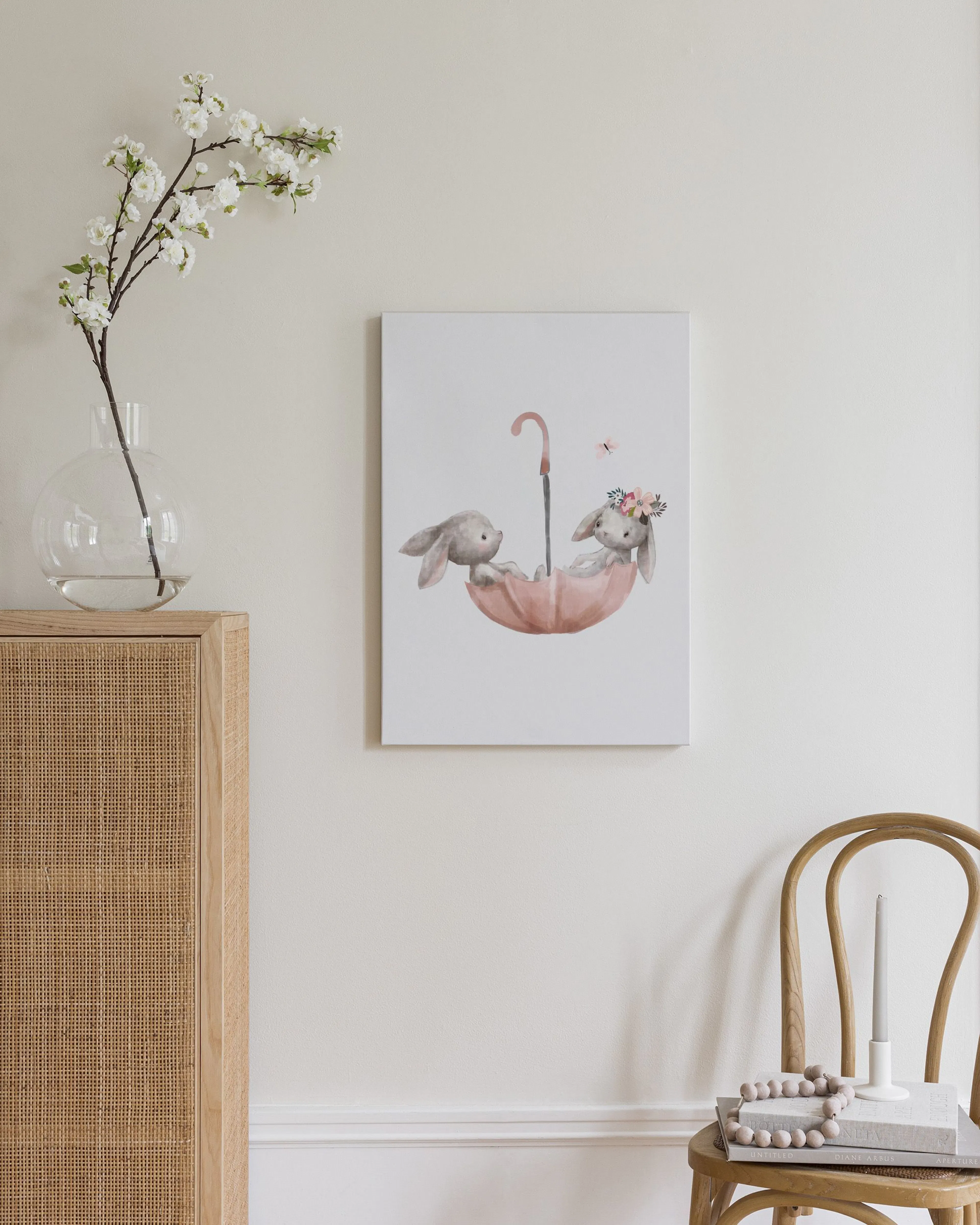 Lienzo con dos conejos bebés en un paraguas rosa, con un conejo con corona de flores, exhibido sobre un mueble de madera.