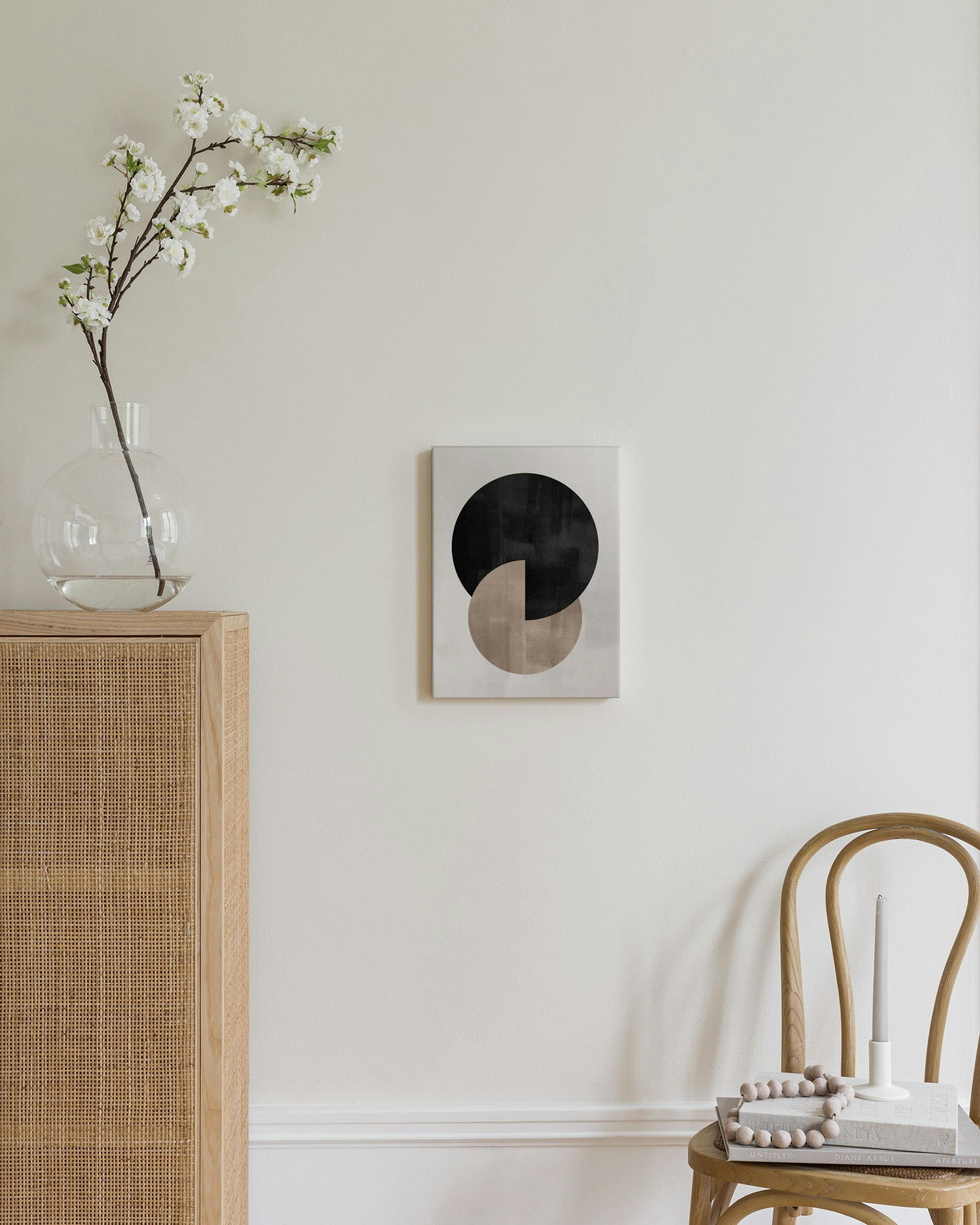 Toile murale abstraite avec un cercle noir et un demi-cercle beige, accrochée au-dessus dune chaise en bois dans un salon modern