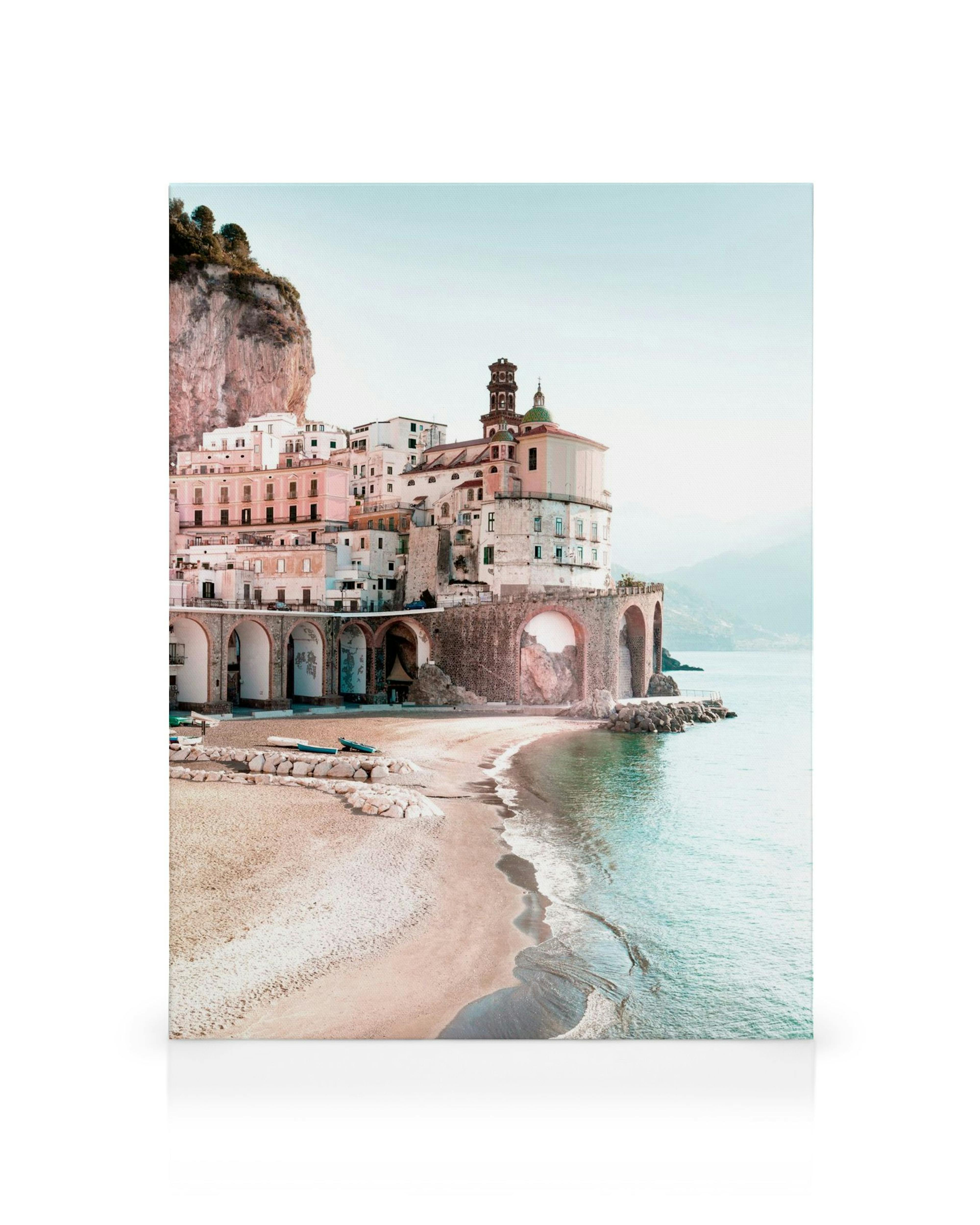 Toile dune plage de sable clair avec des vagues et un village italien coloré adossé à une falaise.