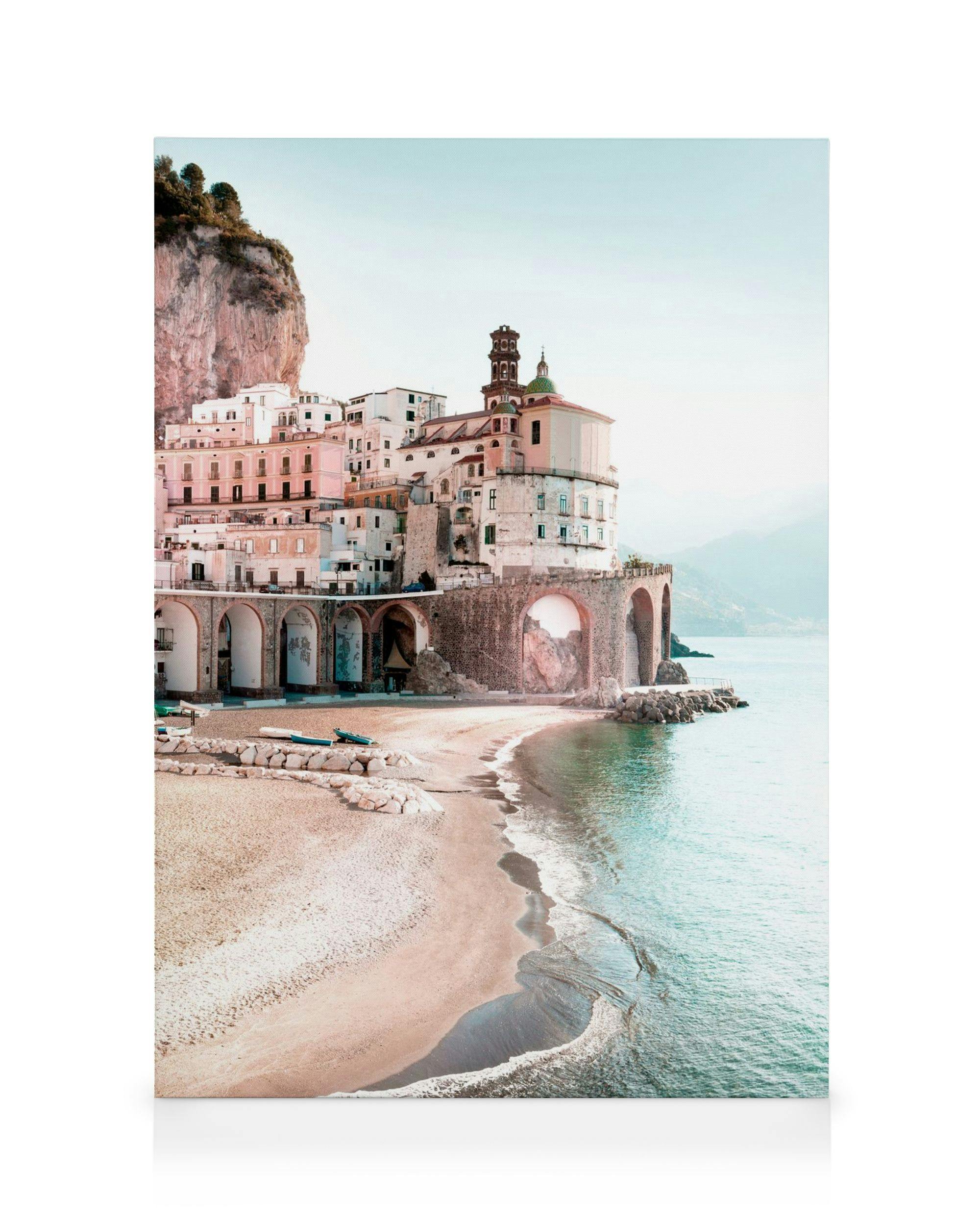 Obraz na płótnie przedstawiający brzeg morza z piaskiem i turkusową wodą, z miastem na klifie w tle.