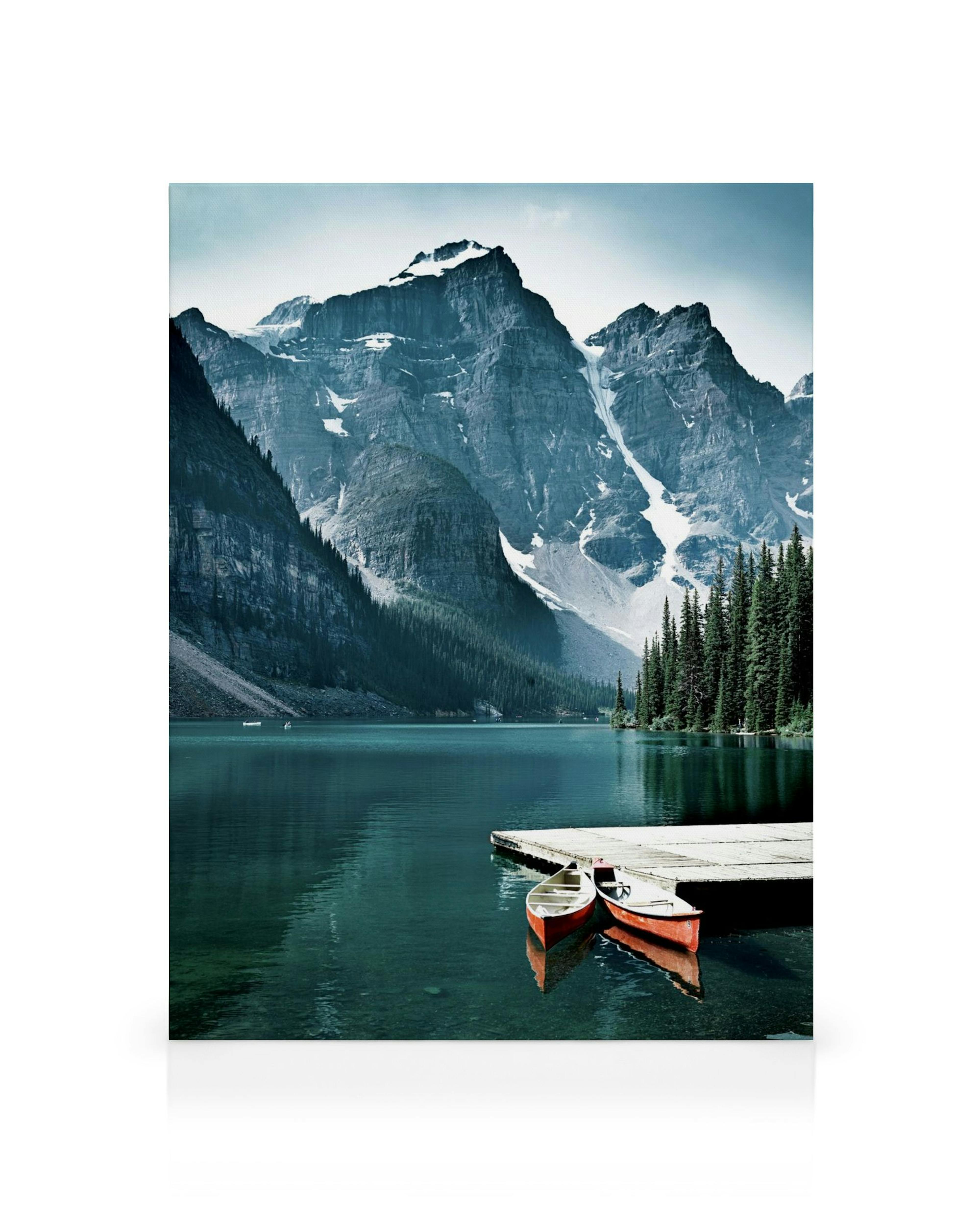 Een canvas van een bergmeer met besneeuwde toppen, groene dennenbomen, een aanlegsteiger en twee boten.