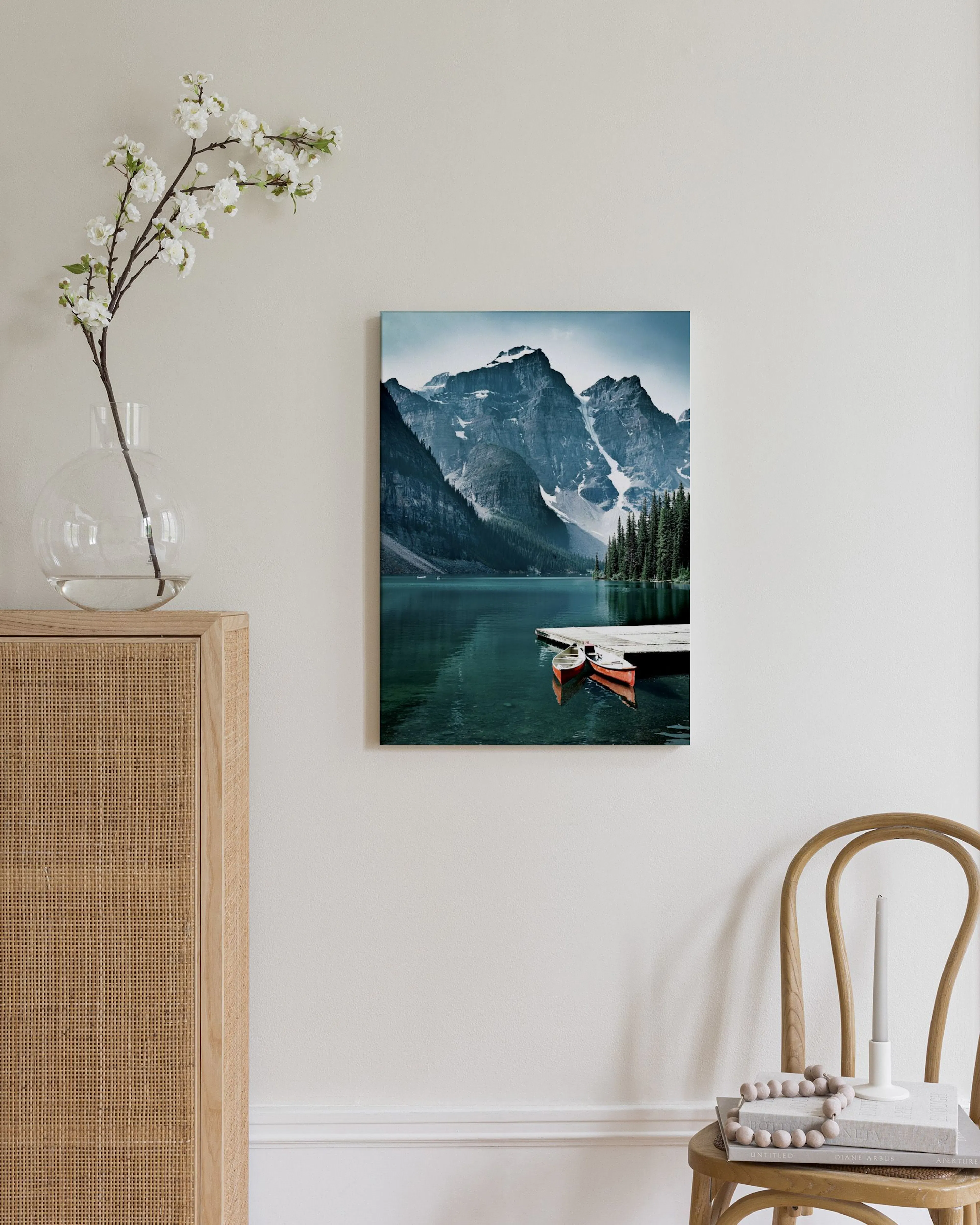 Toile dun lac de montagne turquoise avec des canoës rouges, accrochée au-dessus dun buffet en rotin dans une chambre.