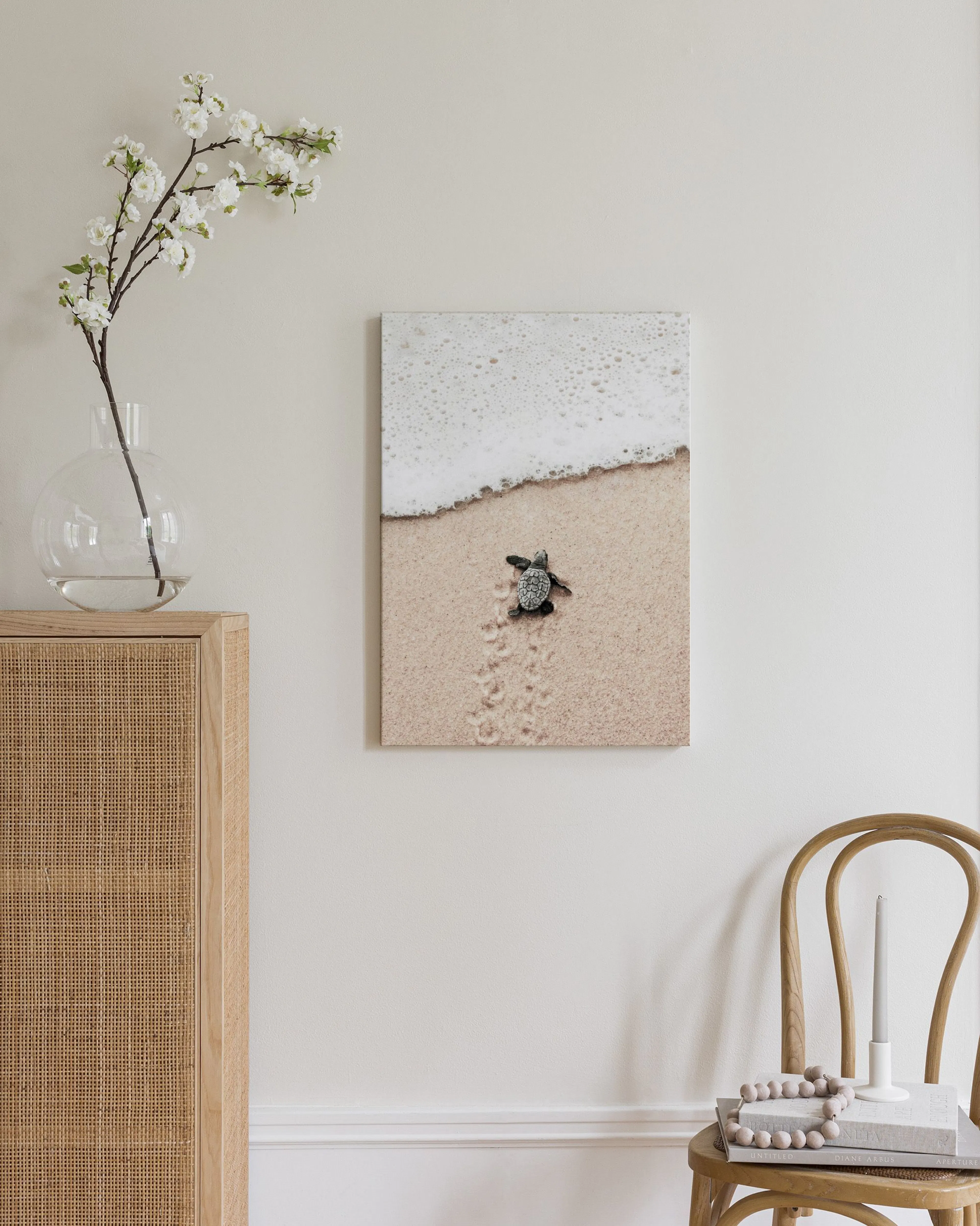Leinwandbild einer Baby-Schildkröte auf Sand mit Wellenschaum, hängt in einem modernen Wohnzimmer über einer weißen Ottomane.